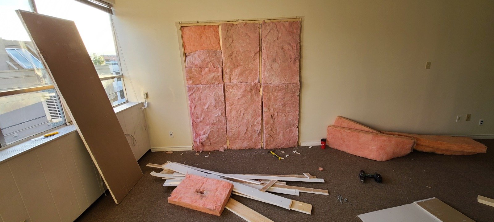 Room under renovation with pink insulation, construction tools, and dismantled wall panels.