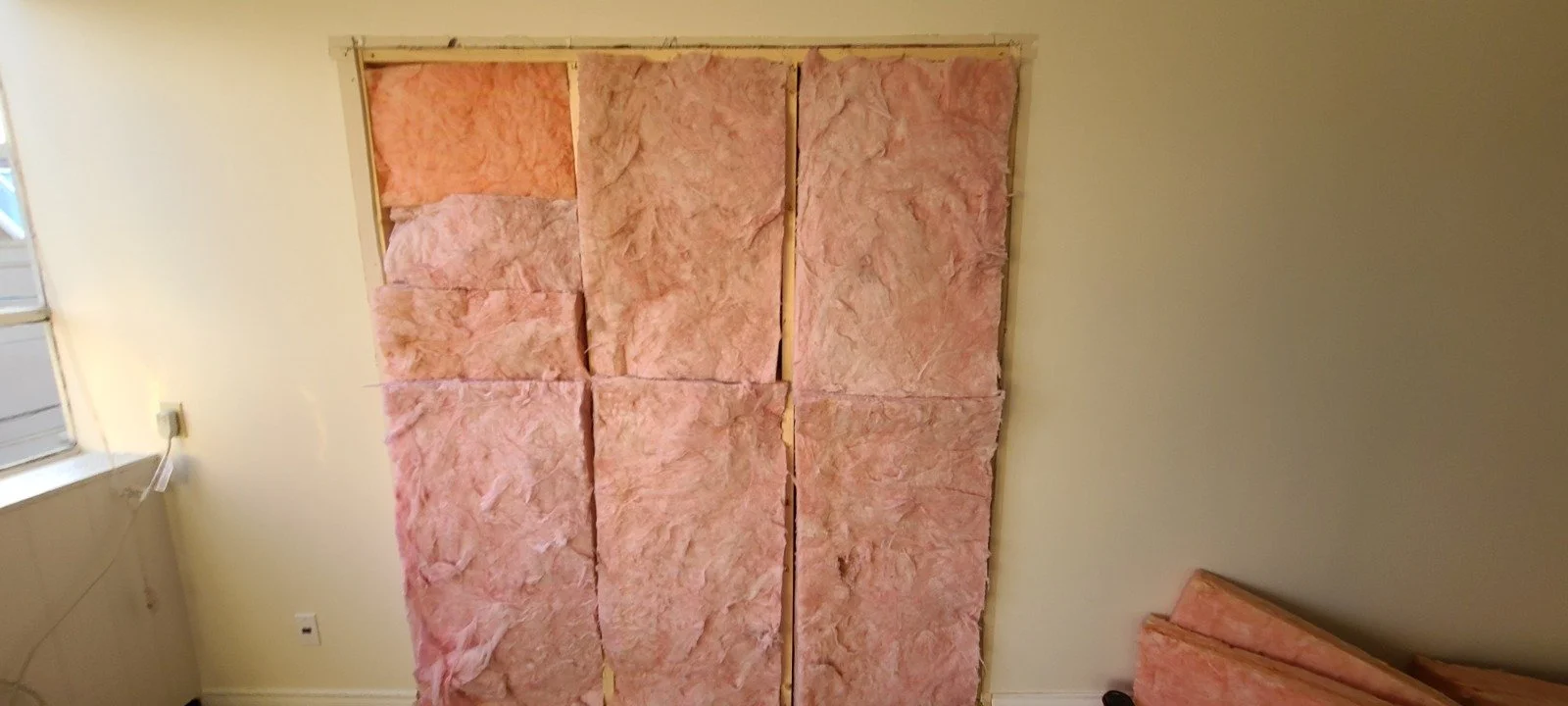 Insulation papered up on a wall with a window and electrical outlet visible.