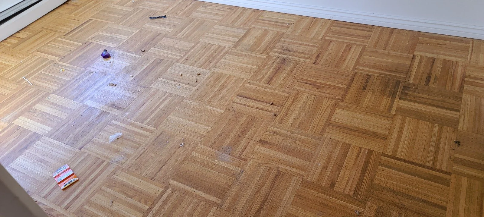 Dirty hardwood floor with scattered trash and debris.