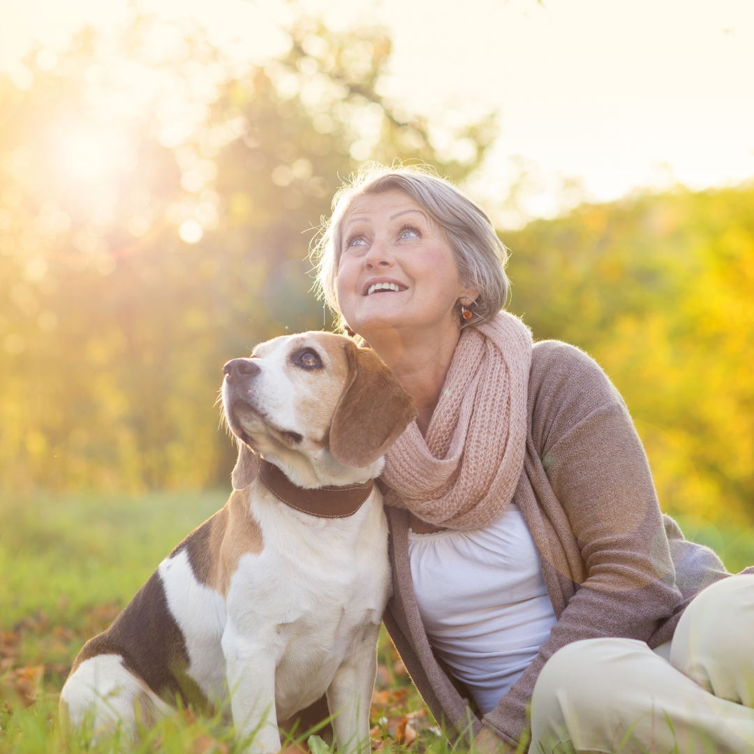 Older Caucasian woman, sitting in the grass with her dog. Both looking up at the sky.