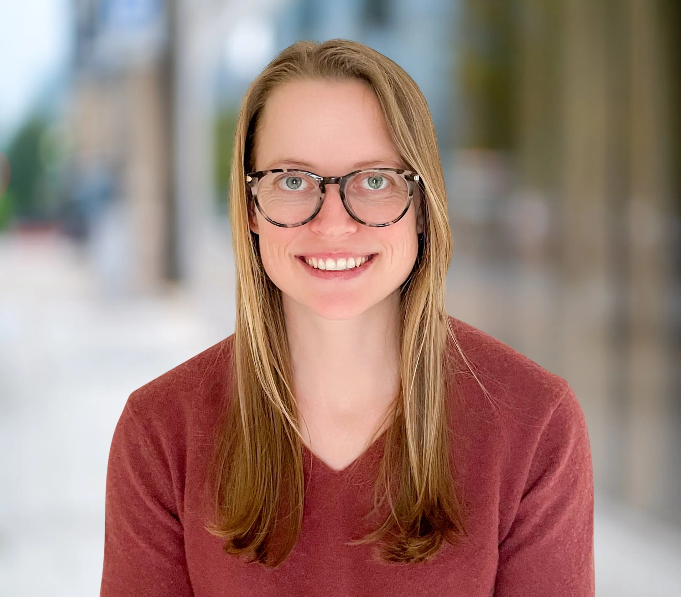 A smiling woman with glasses in a red sweater with blonde hair