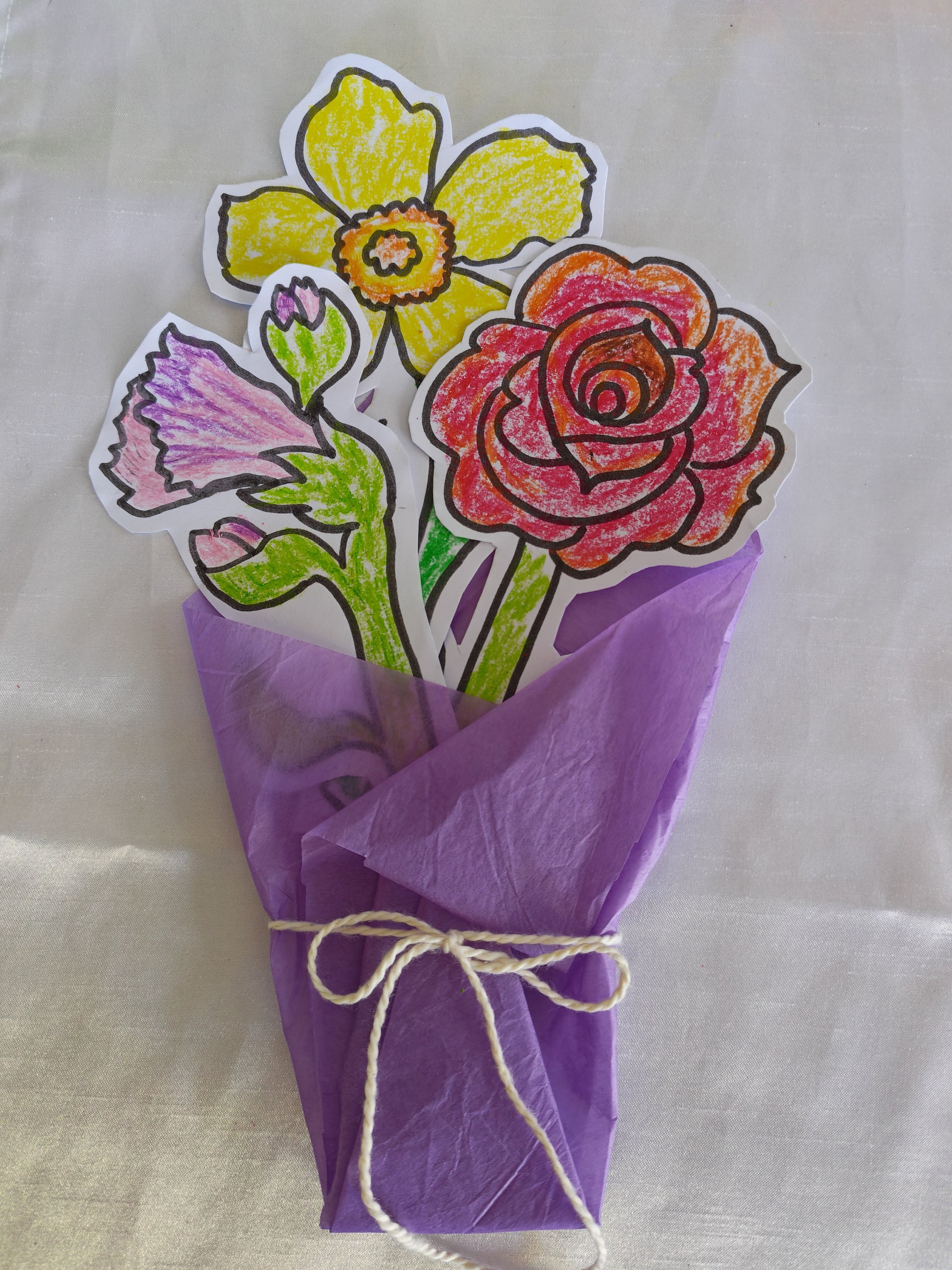 Colorful, hand-drawn flowers made from paper, arranged and wrapped with purple tissue paper, tied with a beige string.