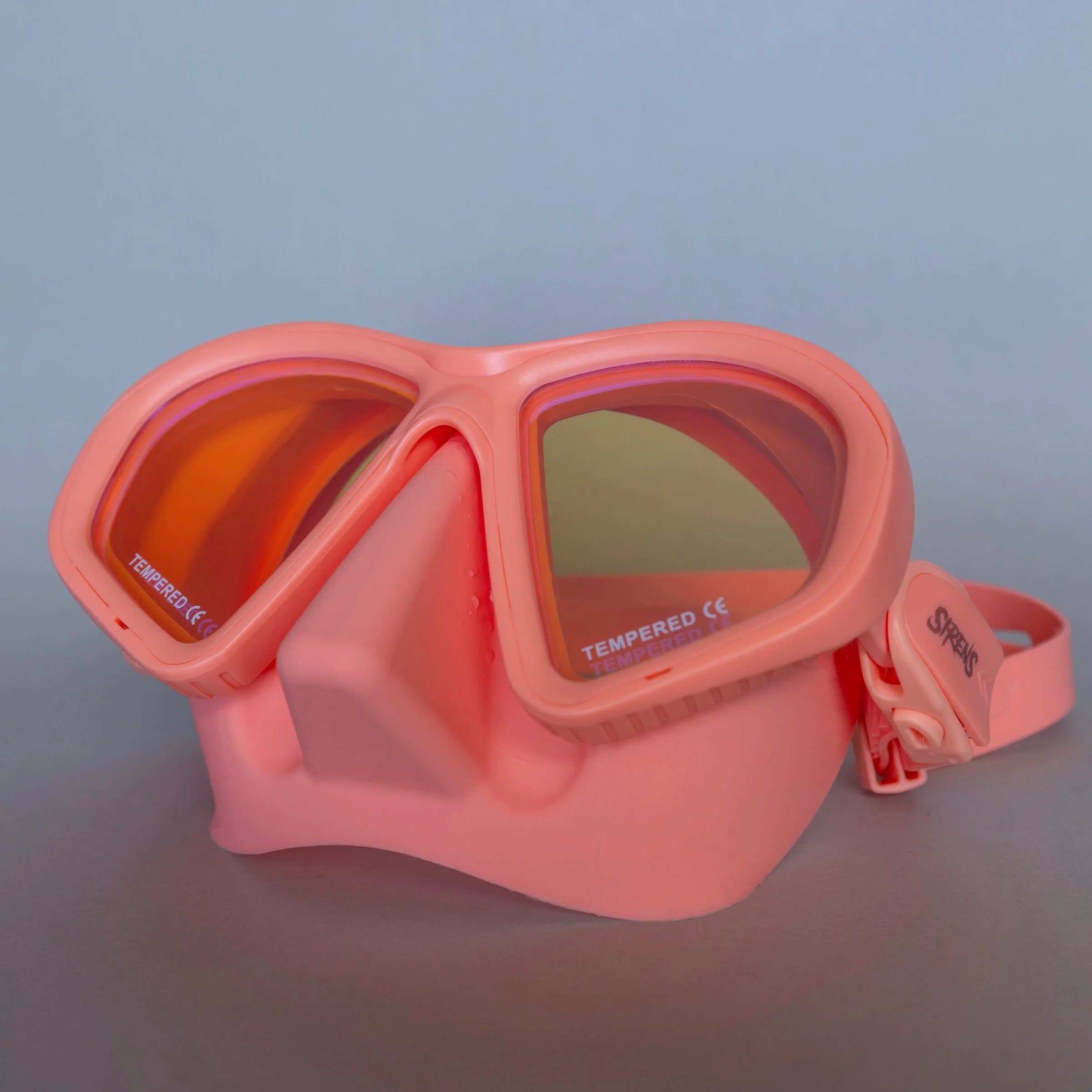 Candy Apple coral-pink Sirens dive mask with warm reflective lenses on a neutral background