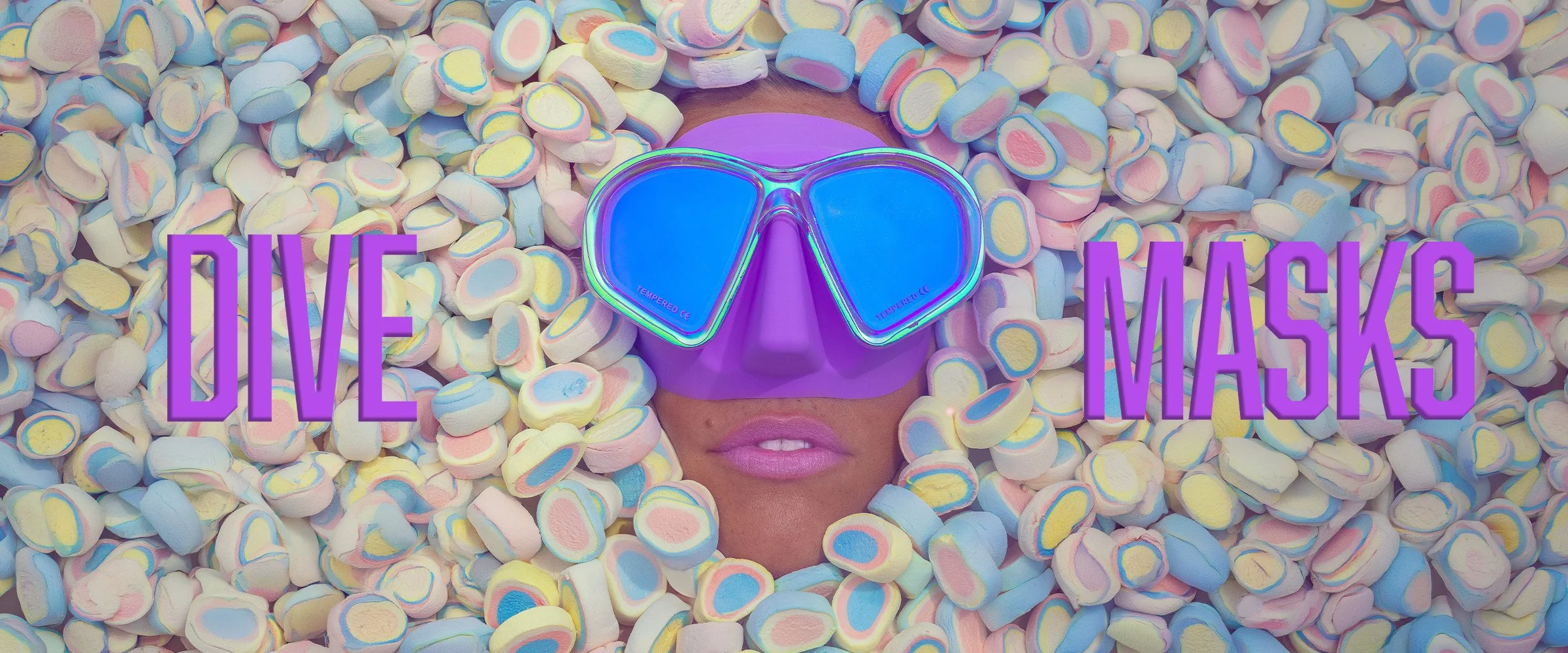 Purple iridescent Sirens dive mask surrounded by pastel sweets, with DIVE MASKS lettering.