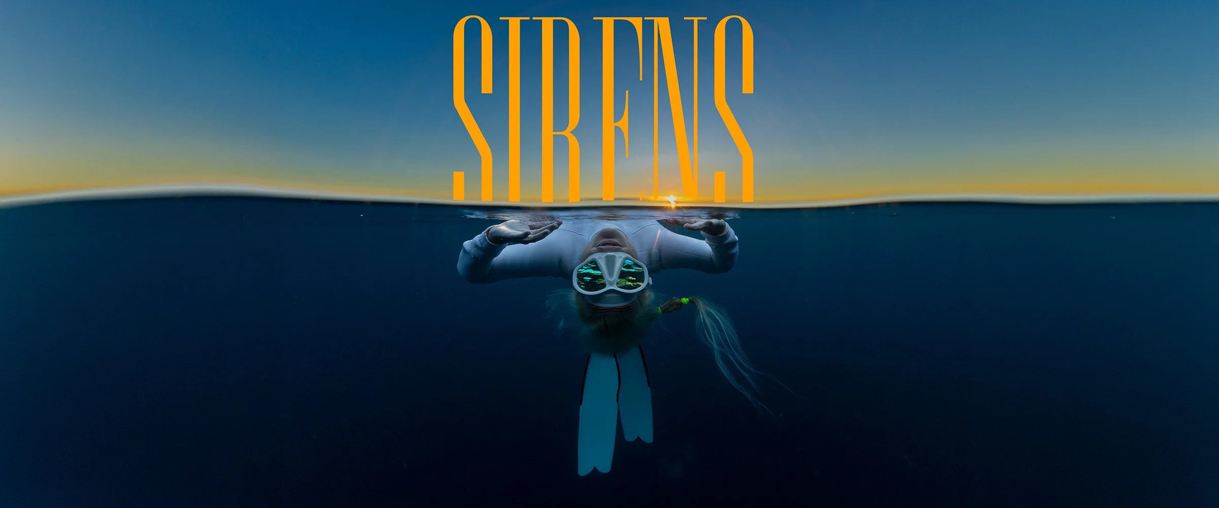 Sirens over-and-under ocean artwork with a masked freediver beneath the sunset.