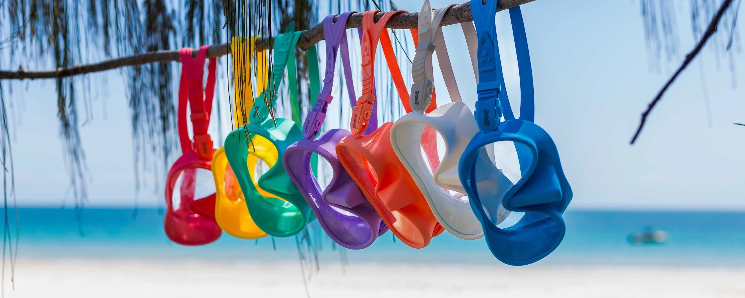 Red, yellow, aqua, lavender, coral, white and blue Sirens dive masks hanging beside the beach.