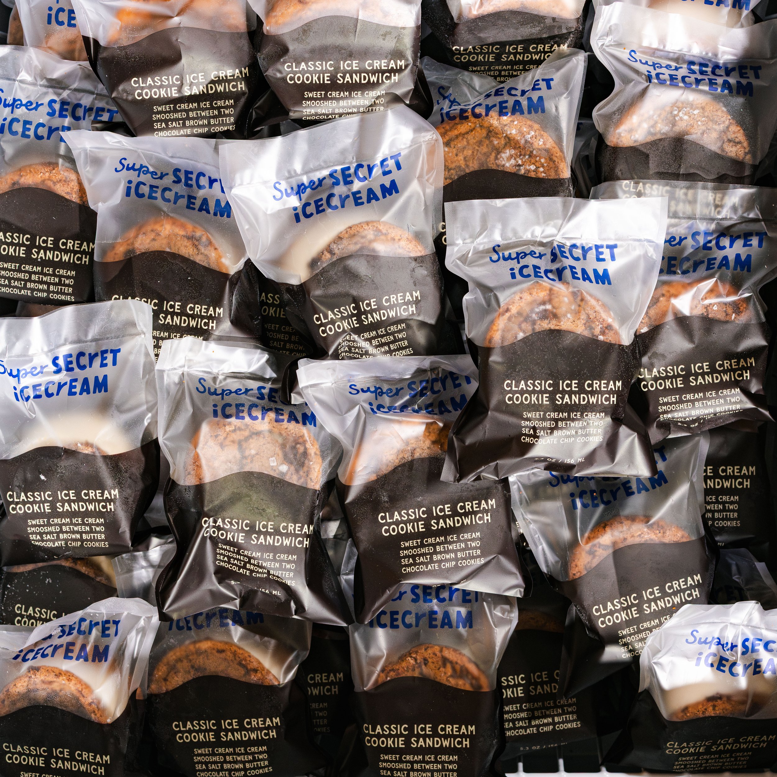 Several packages of ice cream cookie sandwiches with black, white, and clear packaging, featuring text describing the product as "Classic Ice Cream Cookie Sandwich" with flavor details like "Sweet Cream Ice Cream," "Smooshed Between Two Sea Salt Brow
