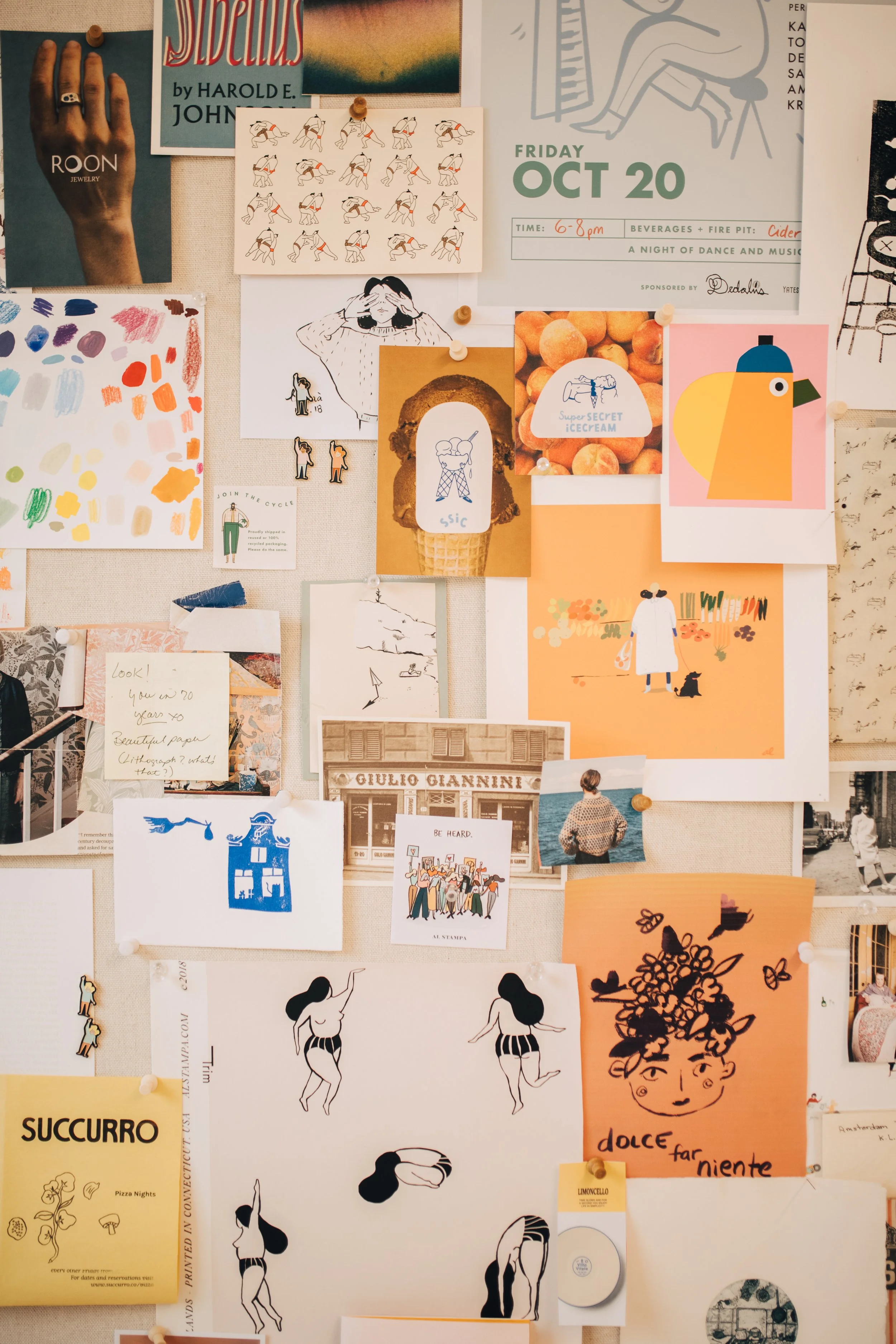 A collage of various art and design pieces on a bulletin board, including illustrations, photographs, posters, and notes, with some images pinned with thumbtacks.