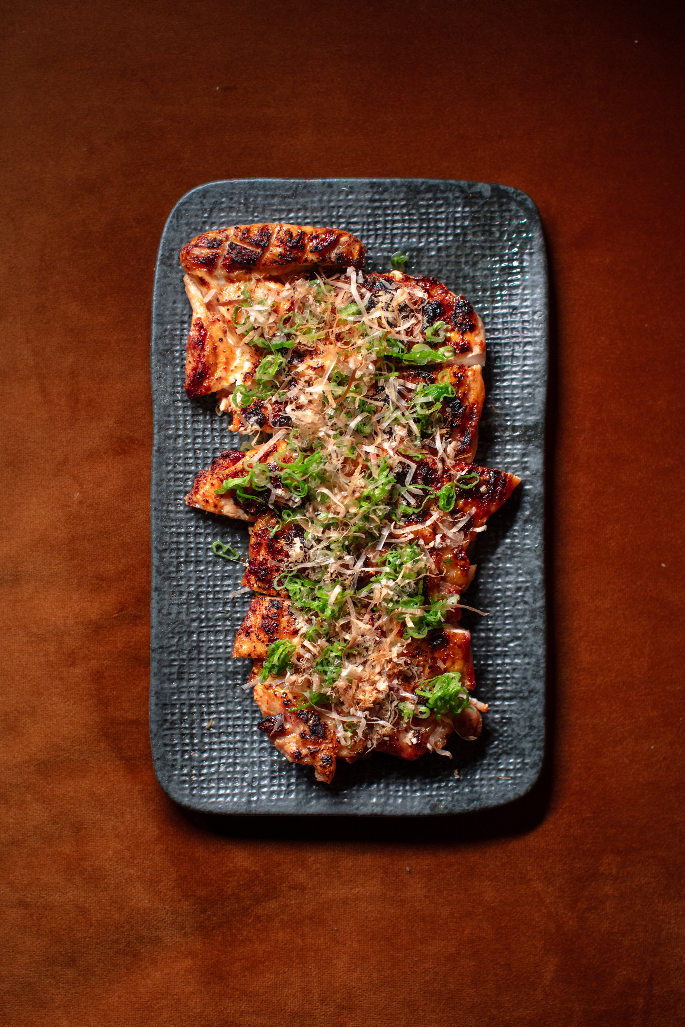 Grilled dish with greens and garnishes on black plate