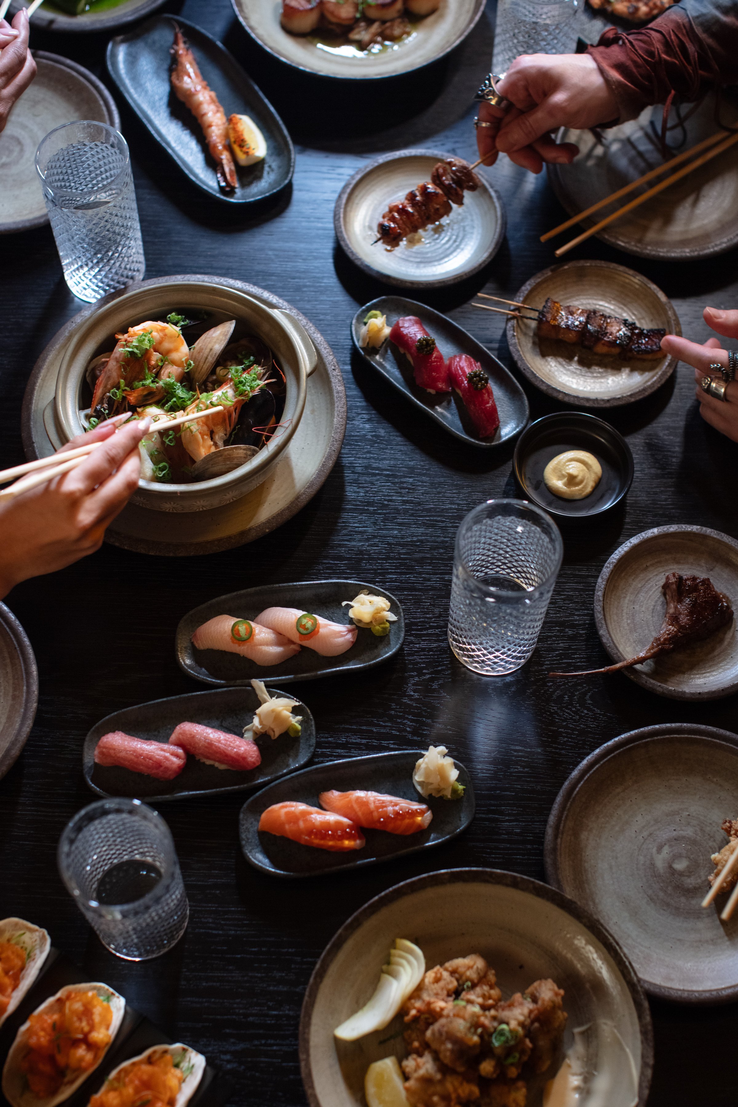 Japanese cuisine spread with sushi, grilled seafood, and skewers on a dark table.
