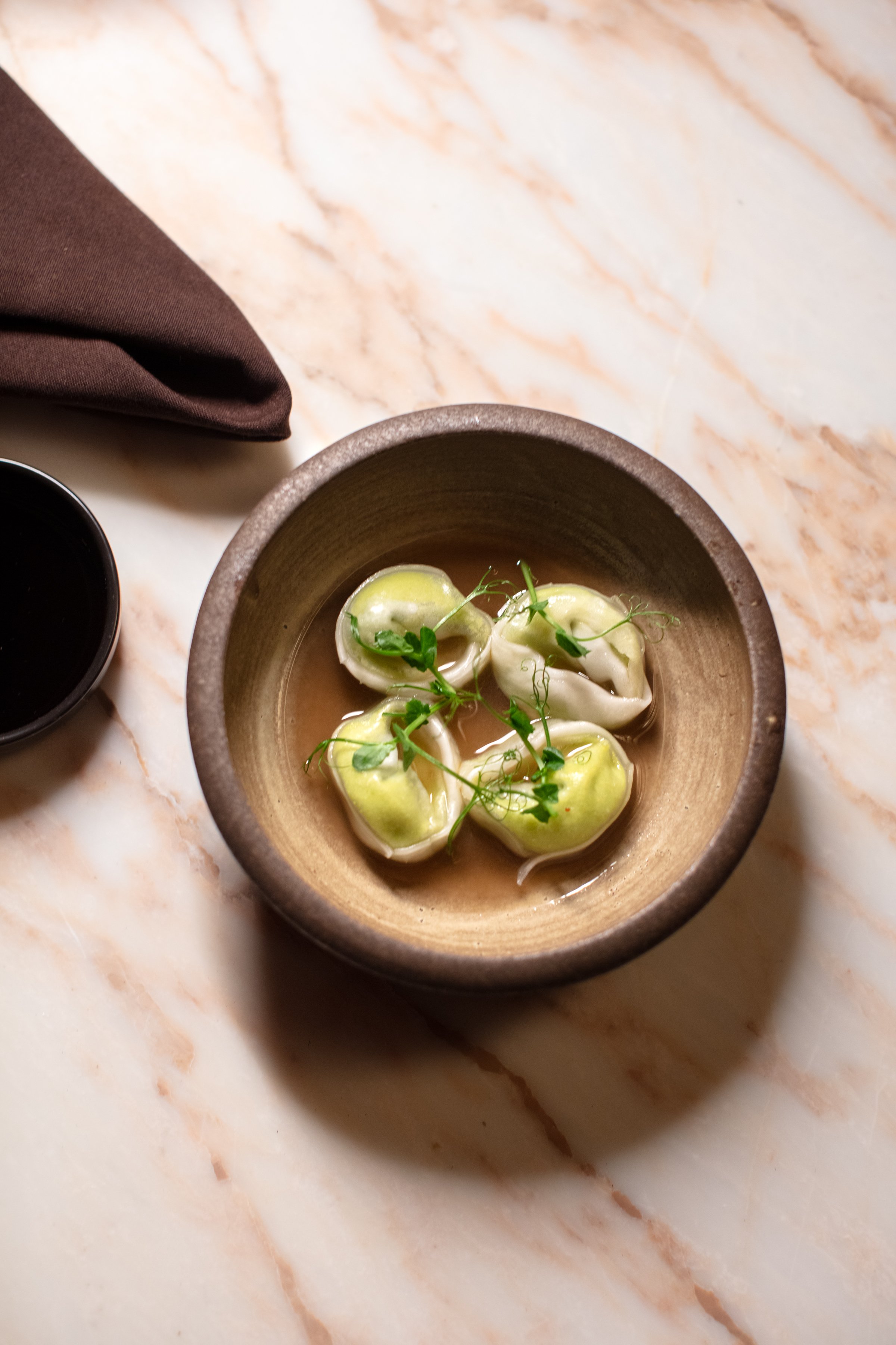 A bowl of dumplings in broth on a marble surface.