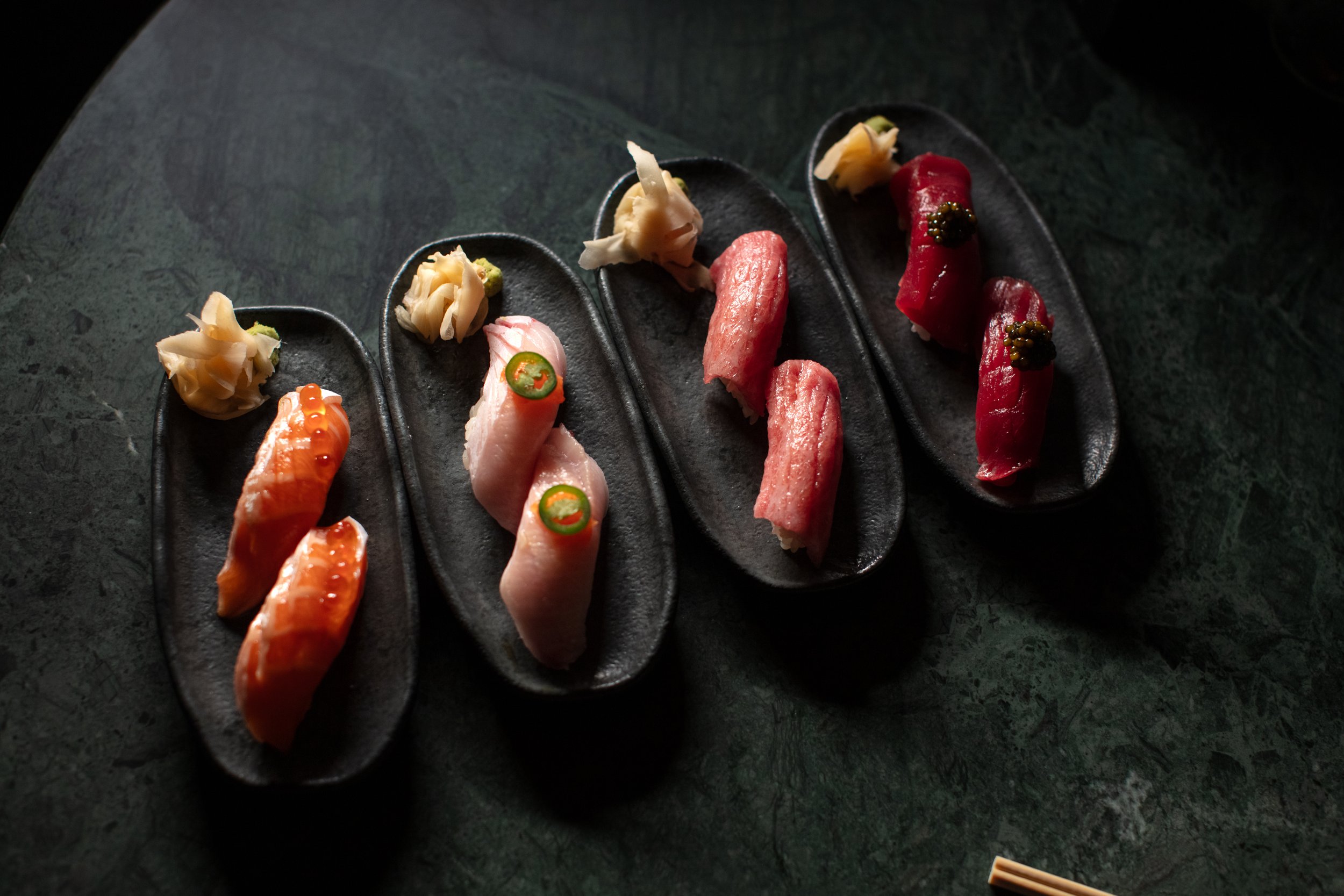 Assorted sushi nigiri on black plates with pickled ginger and wasabi.