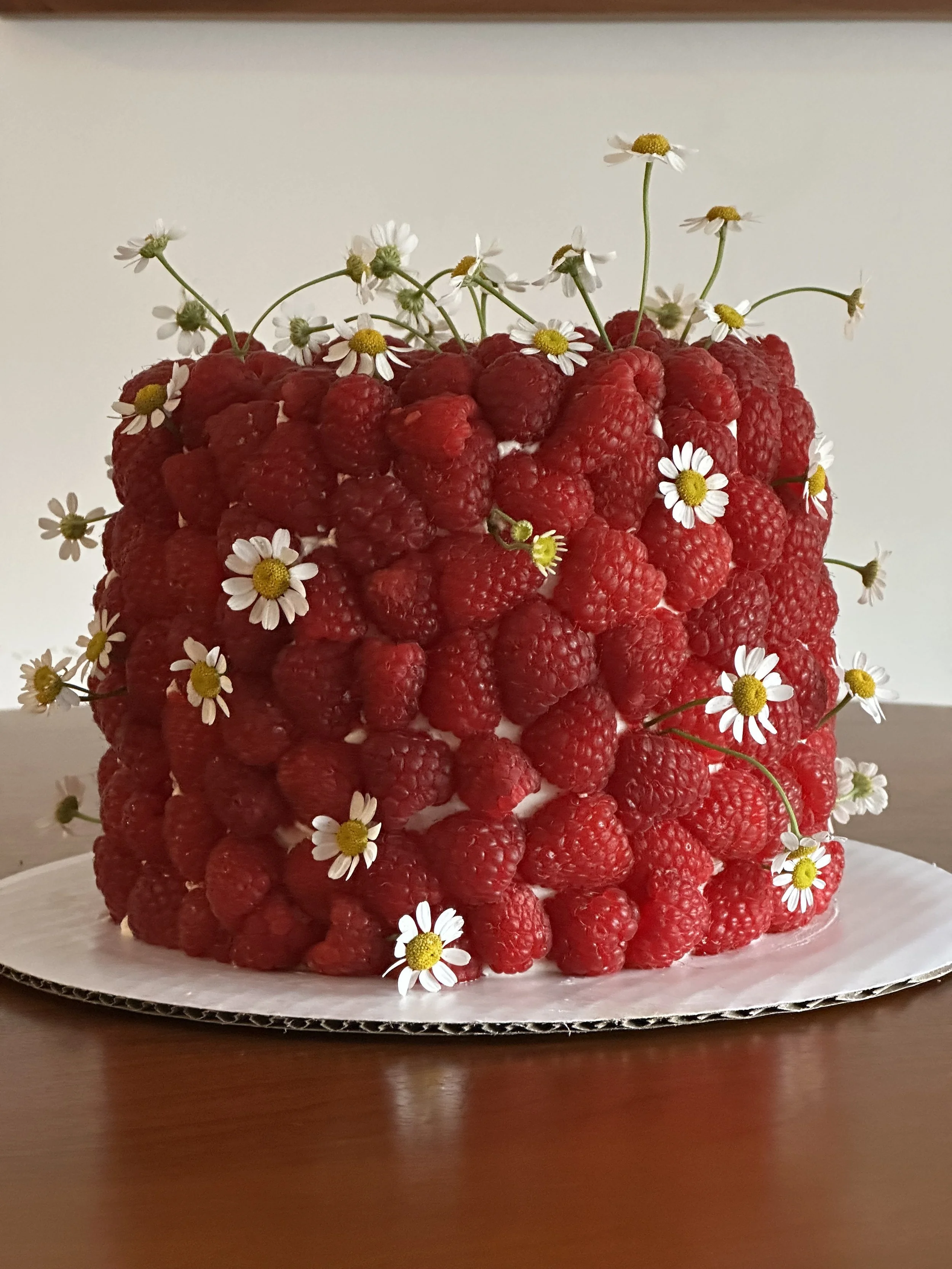 6" cake covered in fresh raspberries and fresh chamomile flowers