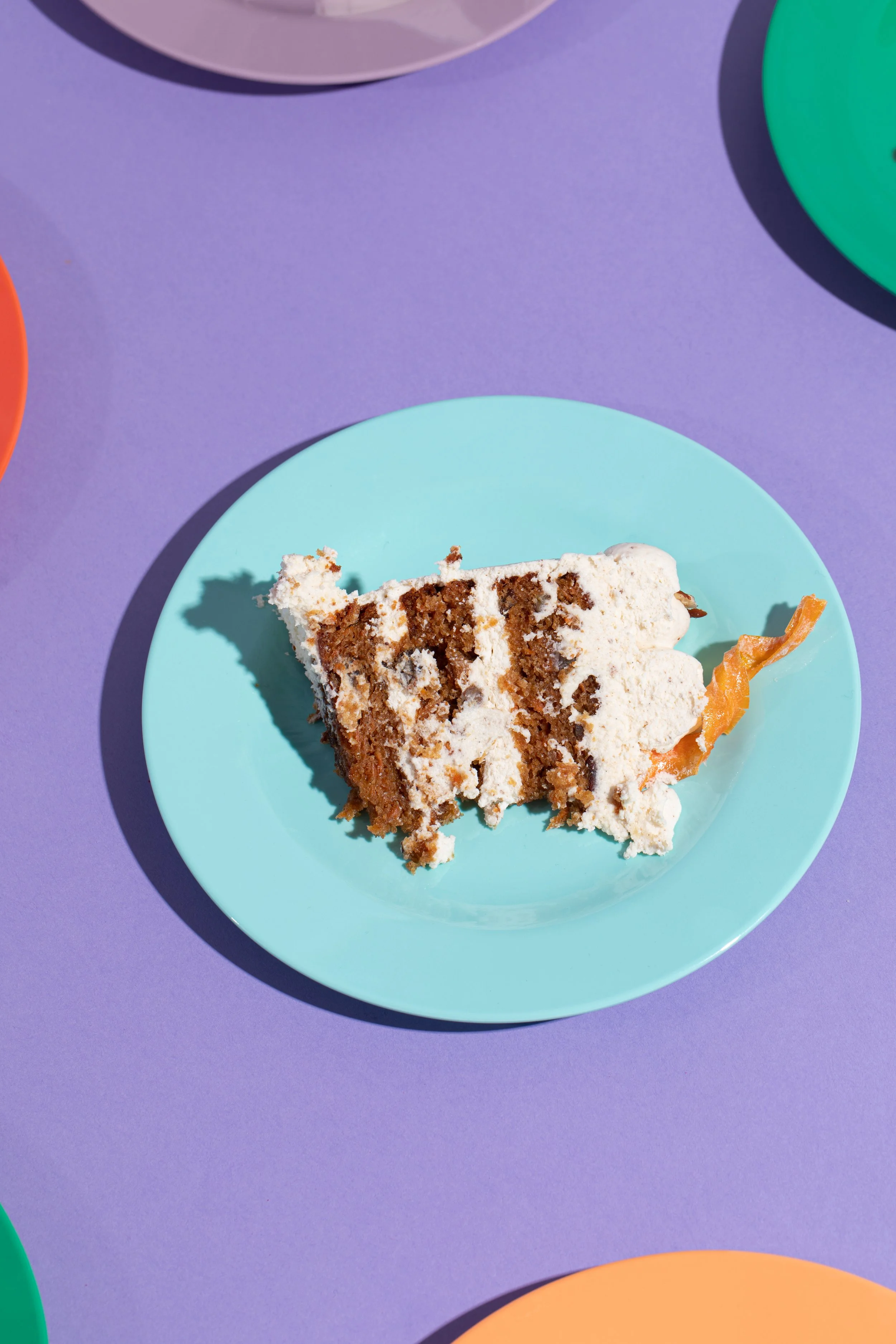 A slice of carrot cake on a bright, light blue plate on a purple background