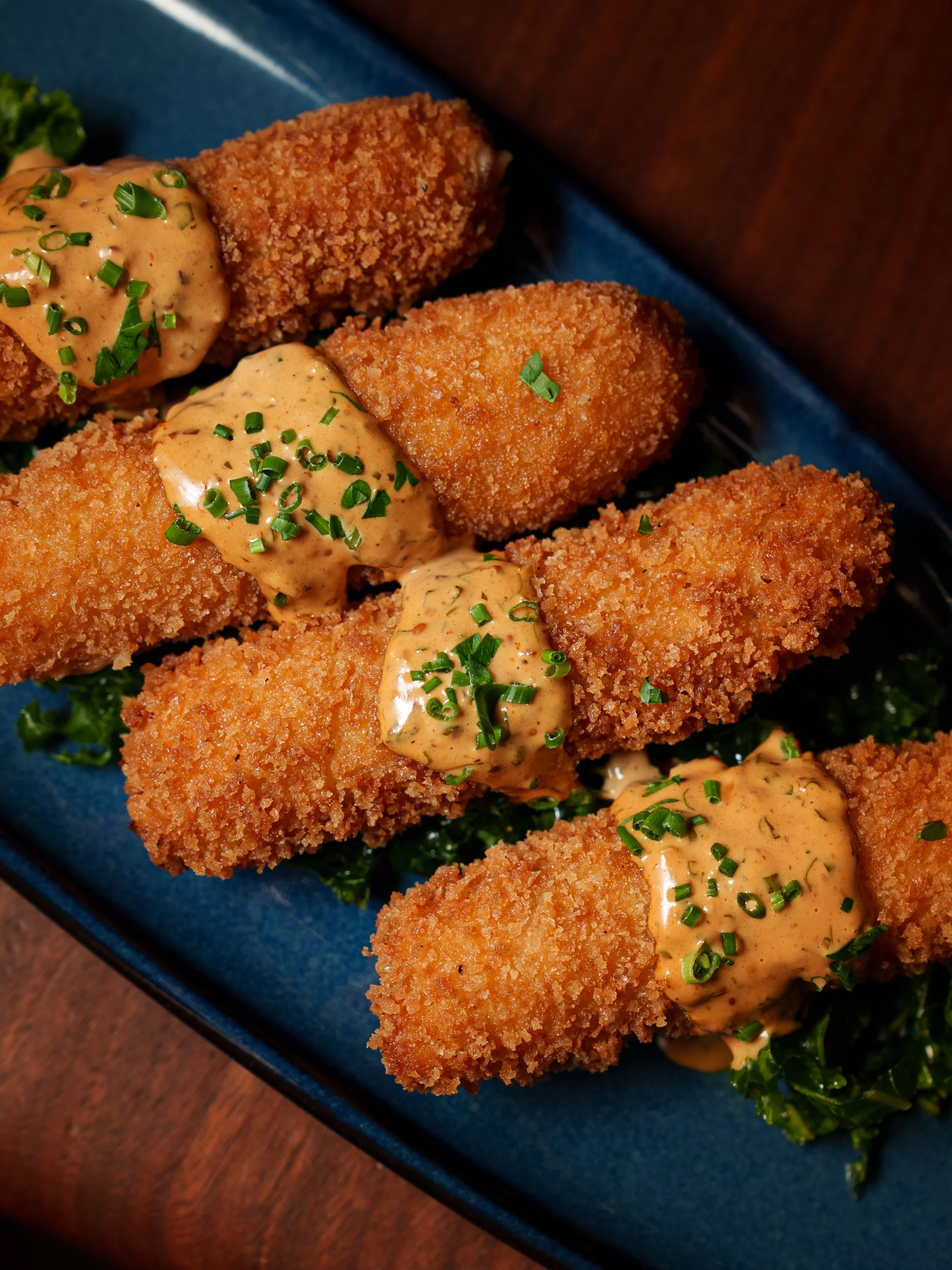Crispy breaded fish fillets topped with creamy, herb-seasoned sauce and chopped green onions, served on a bed of greens on a blue plate.