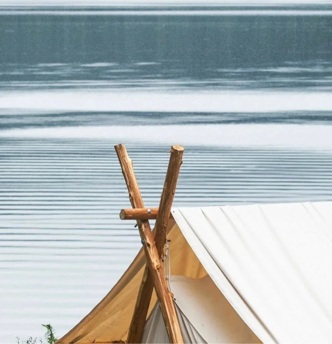 A tent with wooden support poles set up near a body of water with gentle ripples.