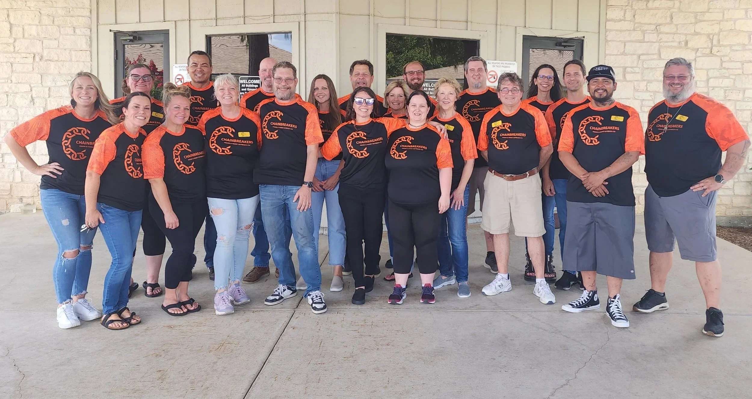 Group of people standing outside a building, wearing matching black and orange shirts with the logo 'CHAINBREAKERS'.