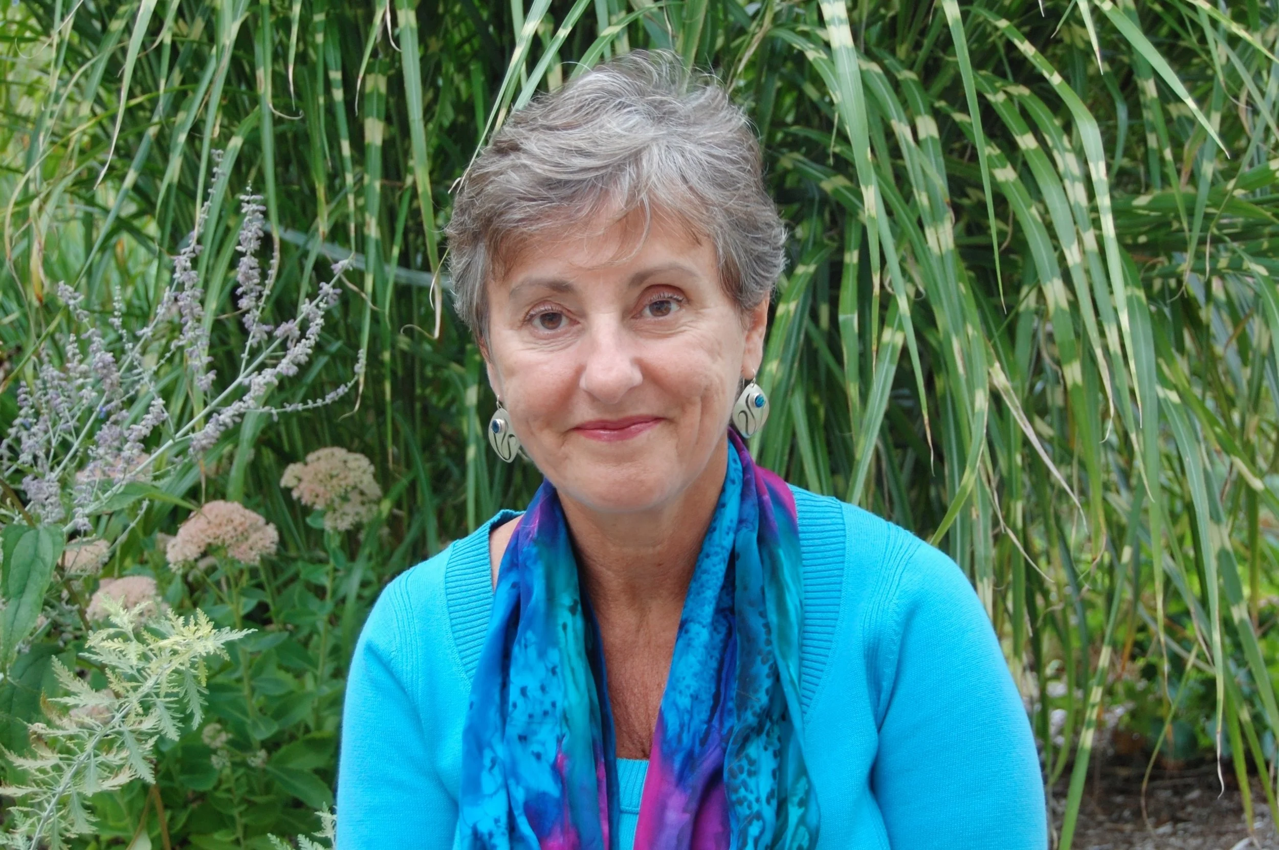 A man with dark, curly hair, glasses, a nose ring, and a beard, dressed in a dark green sweater, looking to the side with a slight smile in an indoor setting.