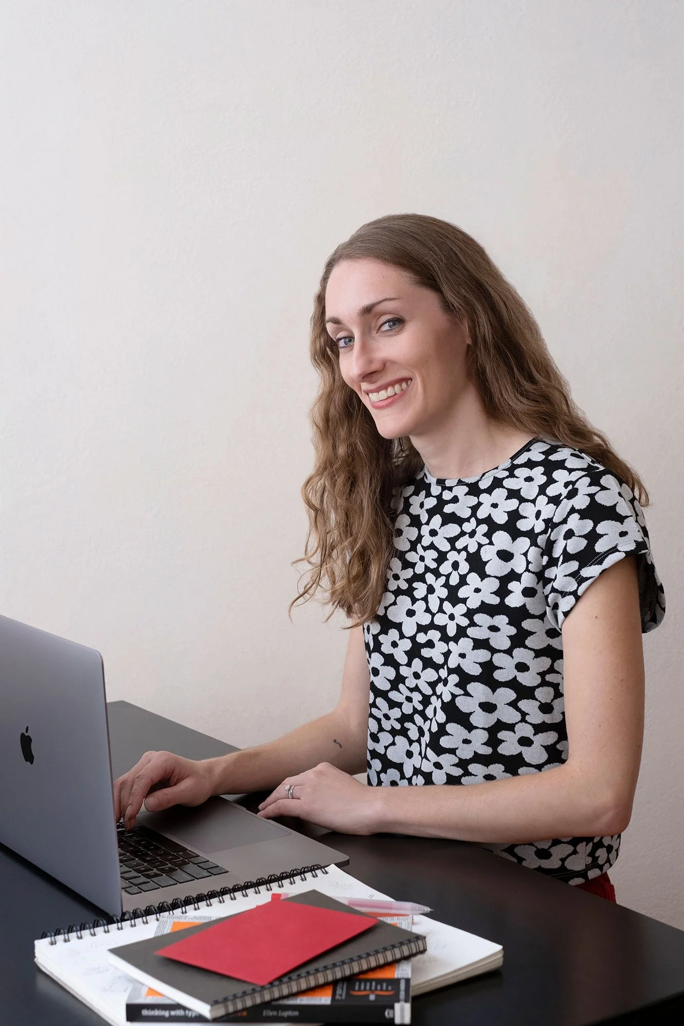 Alyssa Phillips Downey of Amp'd Designs smiling while sitting behind a desk with her hand on the keyboard of a laptop.