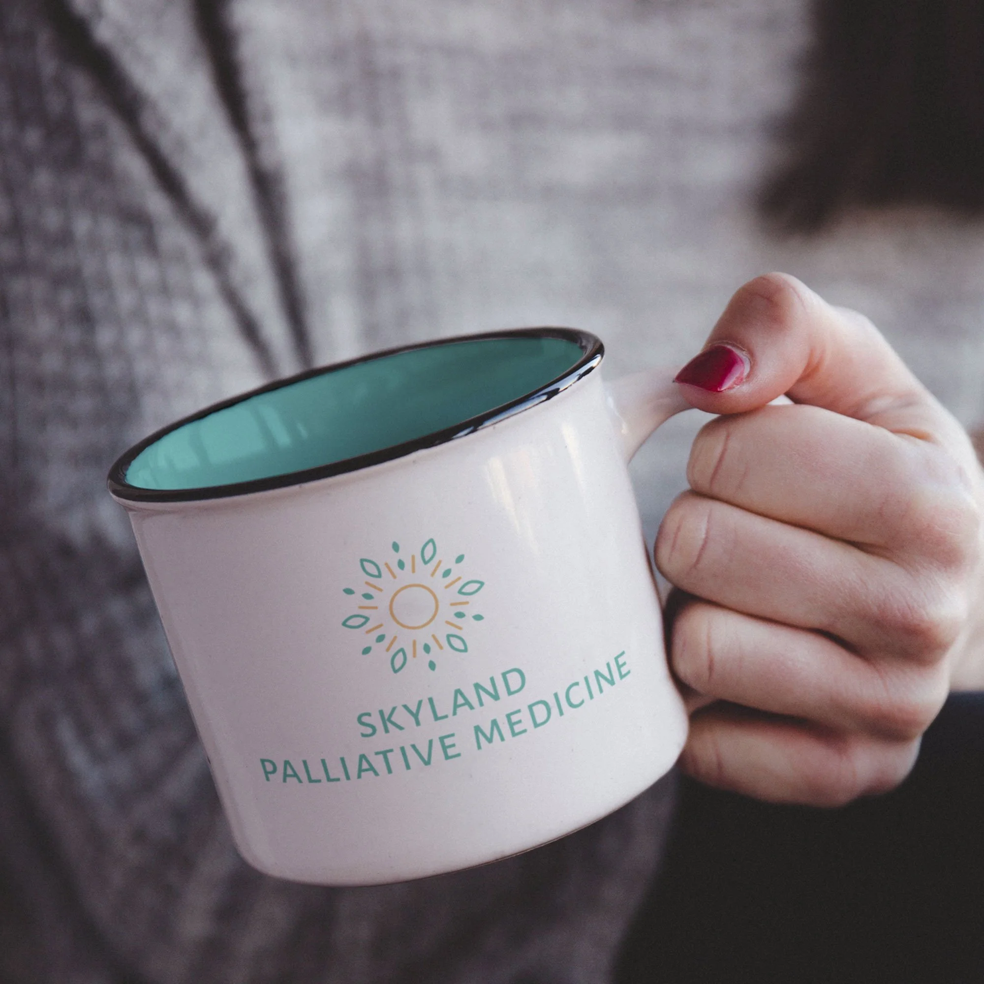 Woman's hand holding a mug with the Skyland Palliative Medicine logo on it