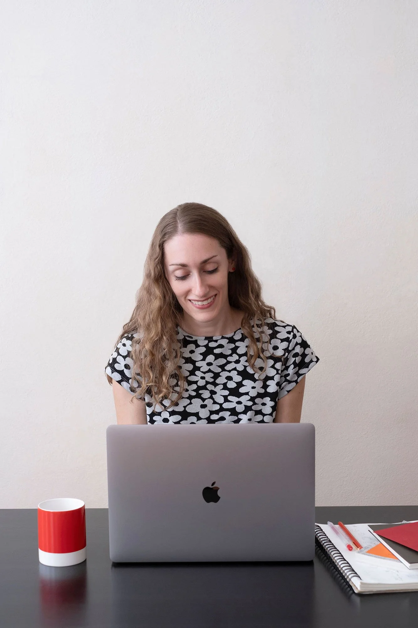 Alyssa Downey sitting at a desk behind an open Apple laptop smiling down at it.