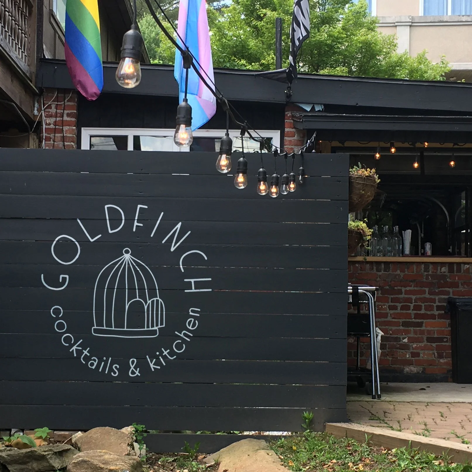 Hand-drawn bird cage logo for Goldfinch Cocktails and Kitchen painted in white on a black fence in Black Mountain, NC.