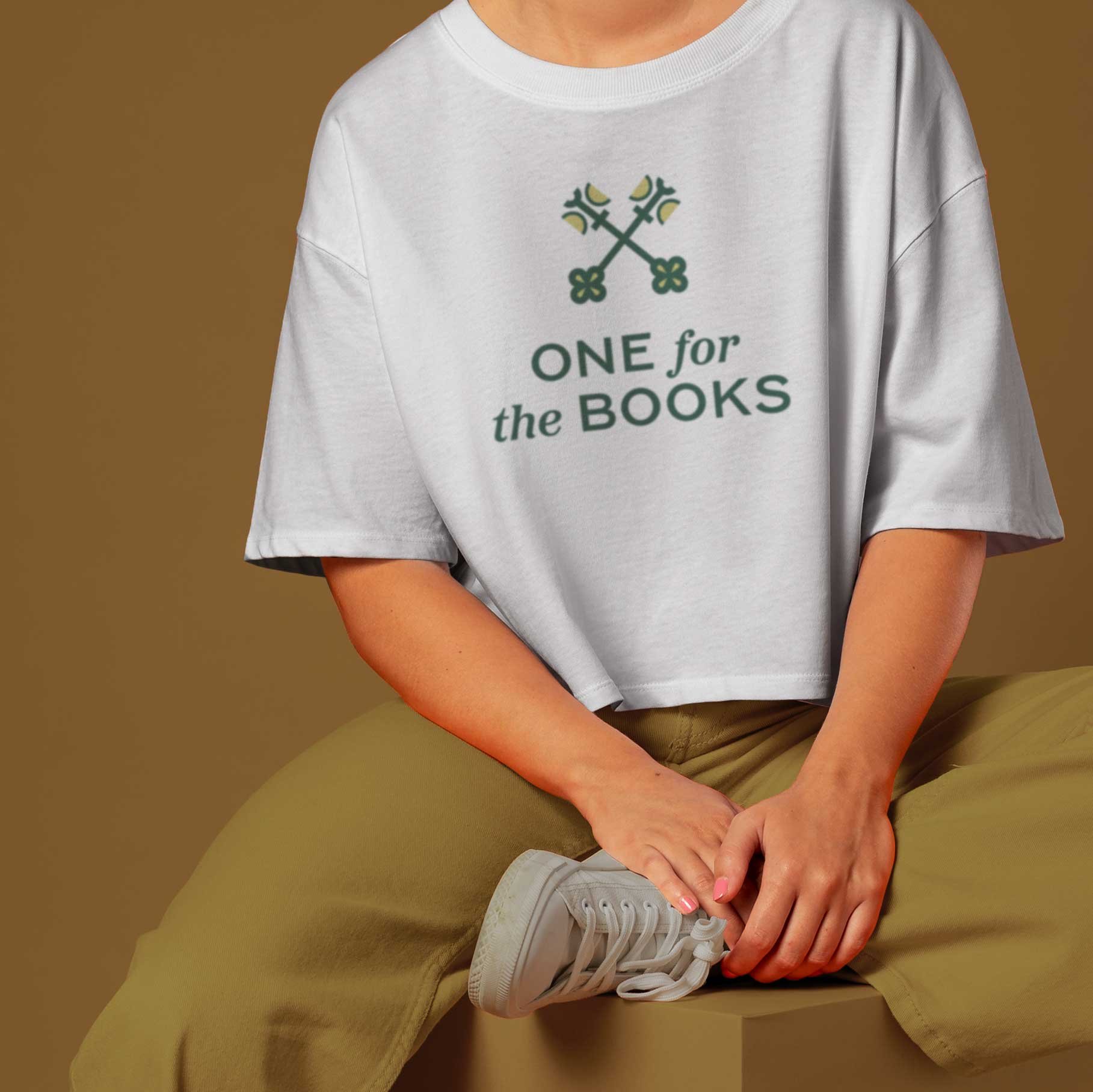 Person sitting cross-legged wearing a white t-shirt with the One for the Books logo on it