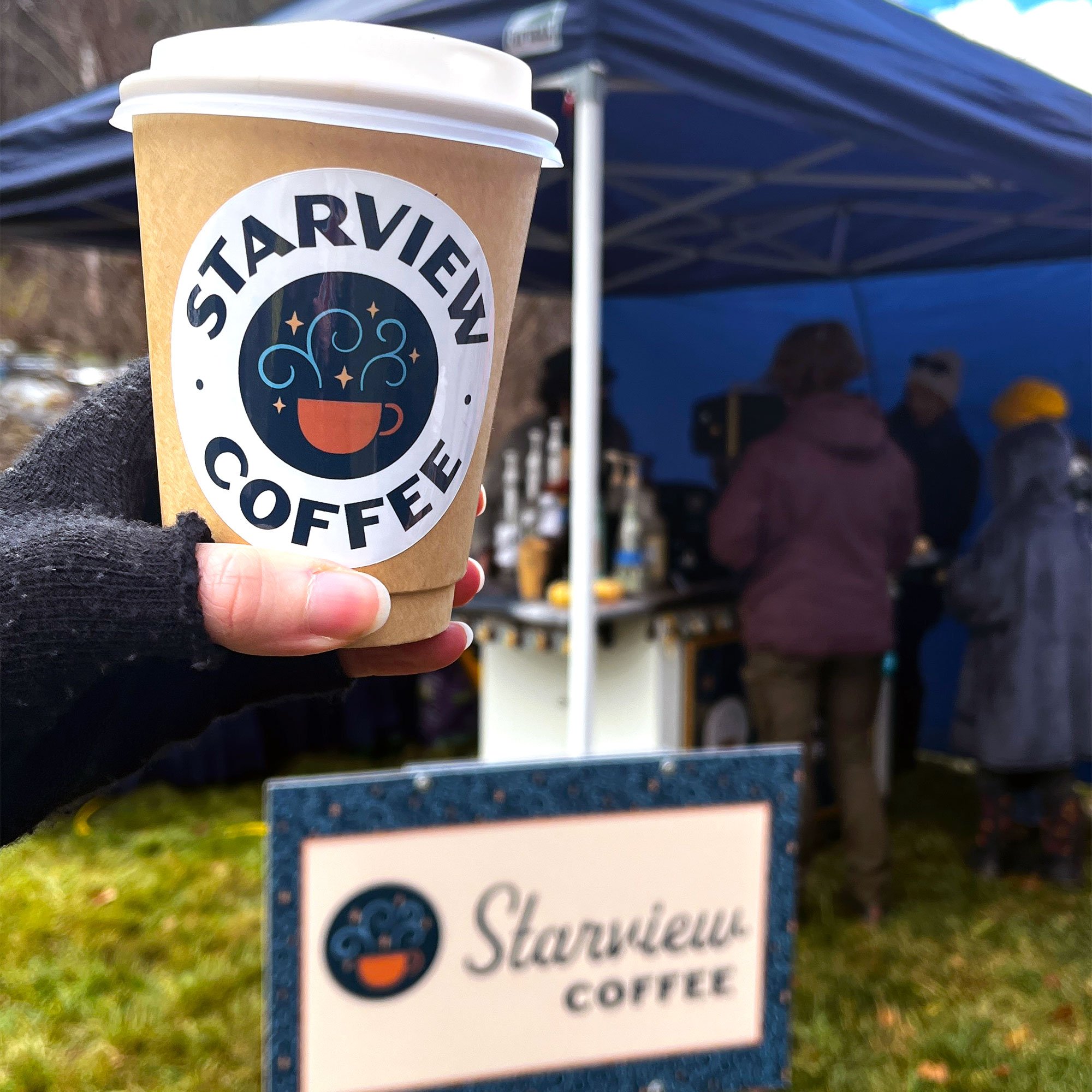 Starview Coffee sticker on a disposable paper cup with their modern, fun logo and custom brand pattern design on a sign in front of a coffee tent at an event in Marshall, NC