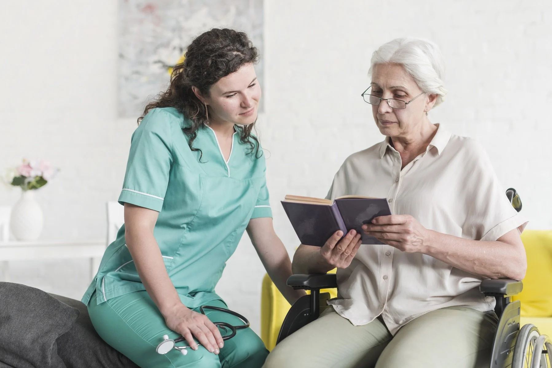 disabled-senior-female-patient-sitting-wheel-chair-reading-book-with-nurse.jpg