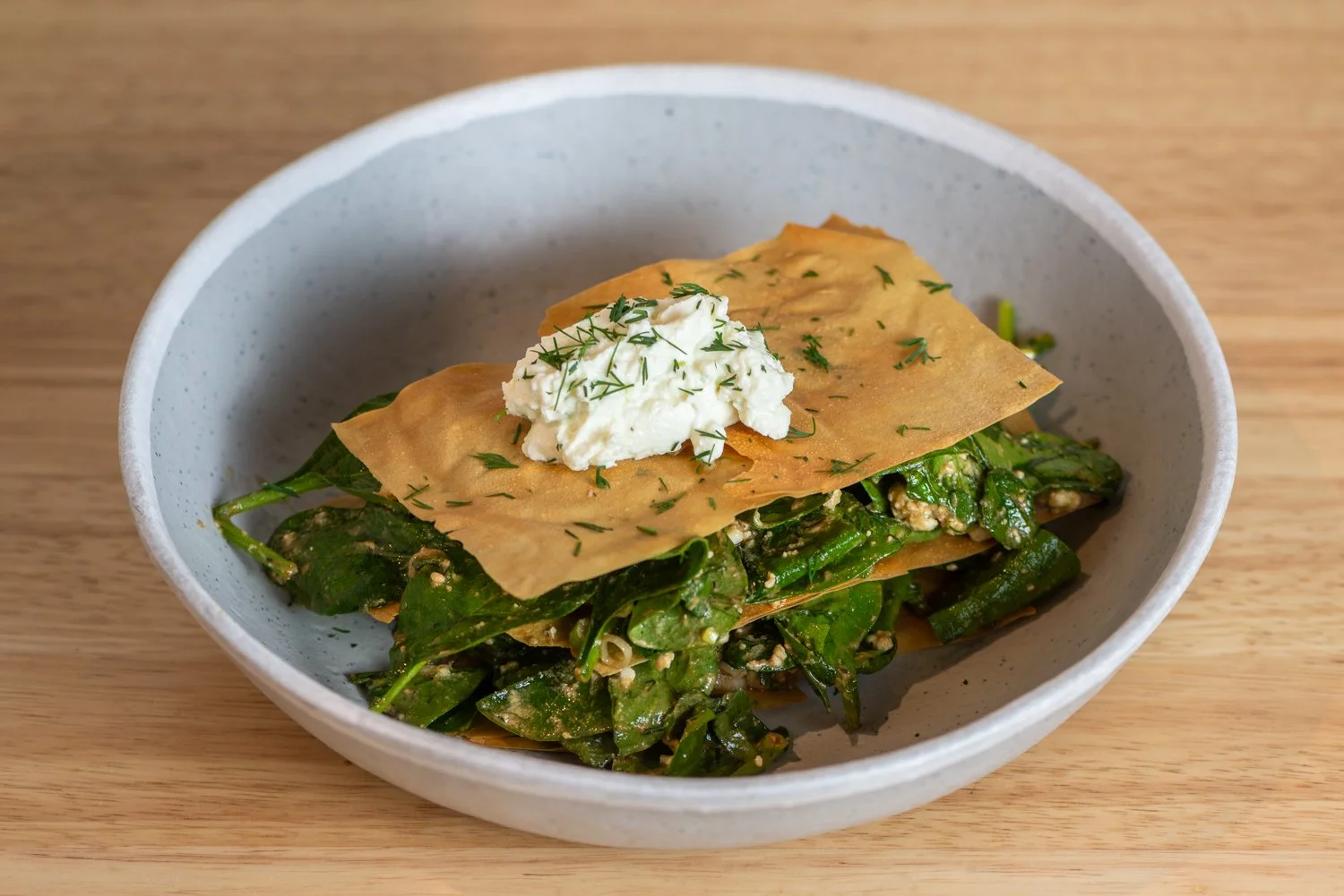 A bowl spinach salad topped with a crispy chip, a dollop of cream, and garnished with herbs.