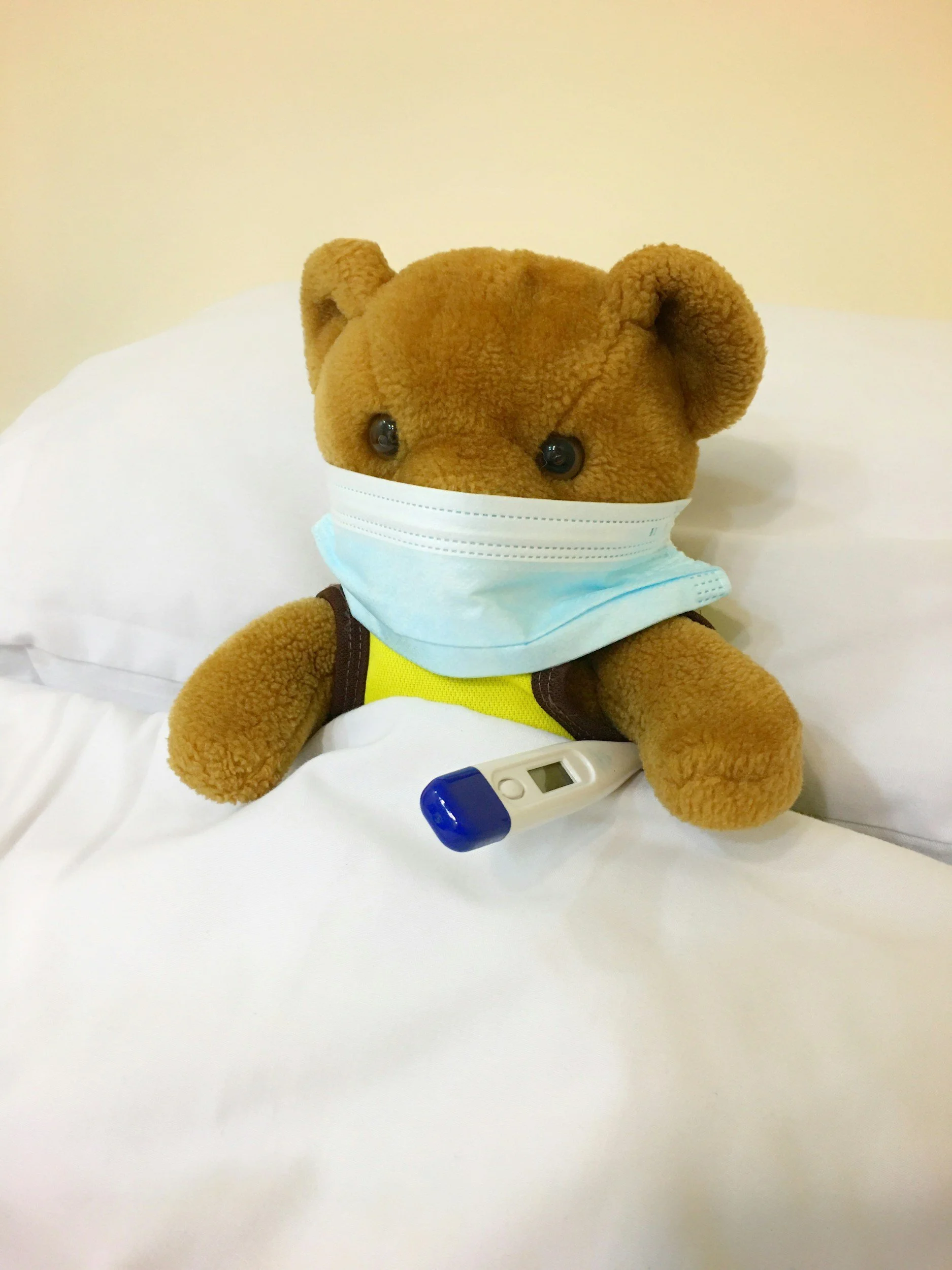 The Mark of Massage Blog | Why Do You Feel Unwell After a Deep Tissue Massage? | teddy bear in bed with a mask and a thermometer under its left arm