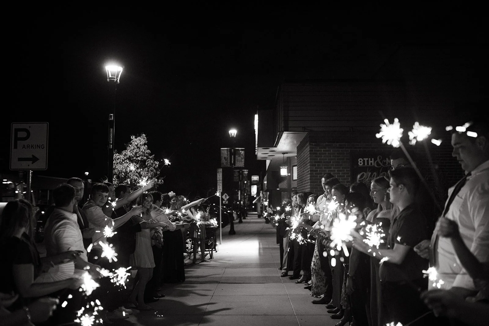 Guests line the Main Street sidewalk with sparklers for a nighttime send-off outside 8th & Main.