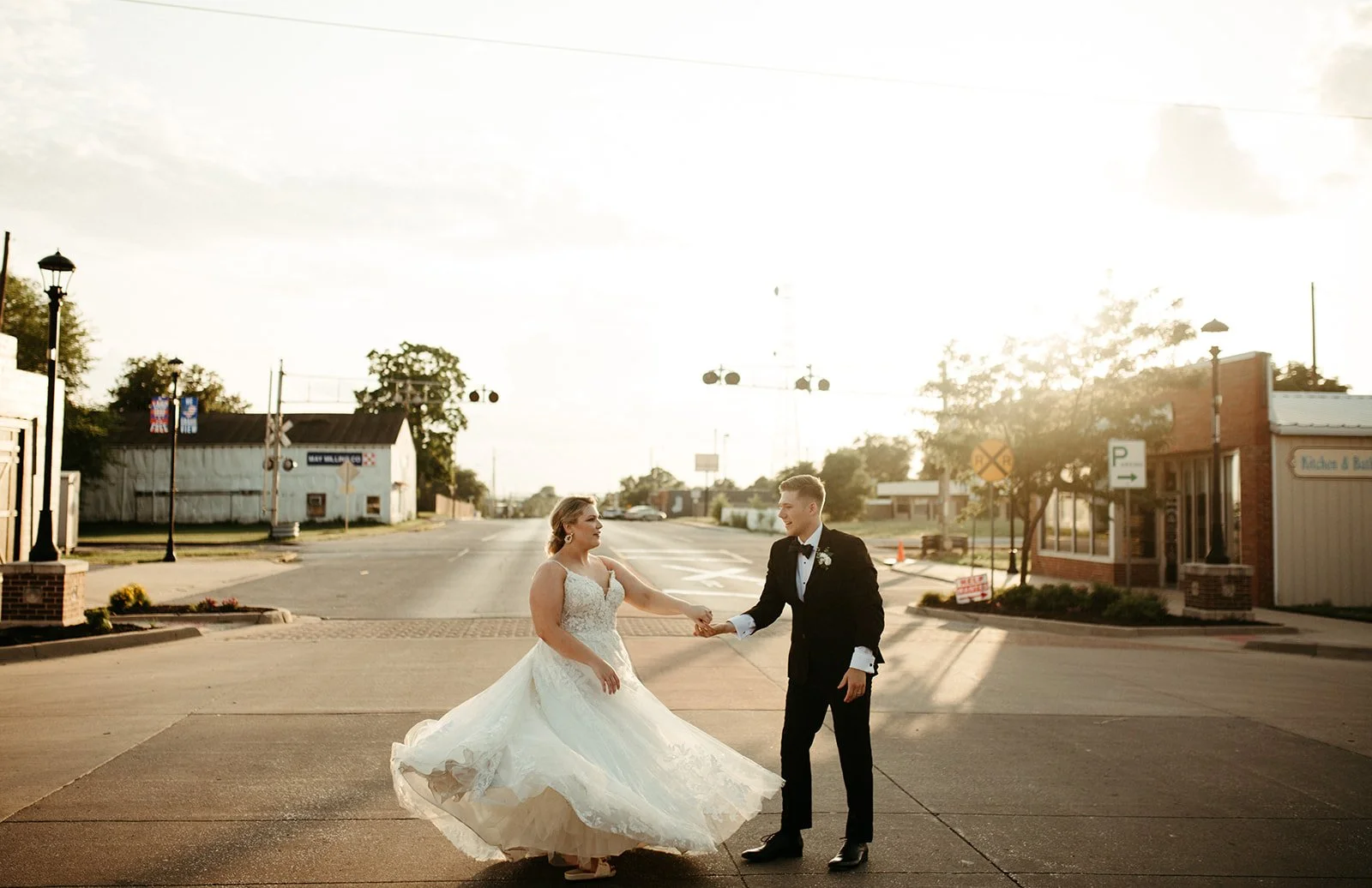 Newlyweds dance at golden hour on downtown Grandview’s Main Street, vintage lampposts and a railroad crossing behind them.