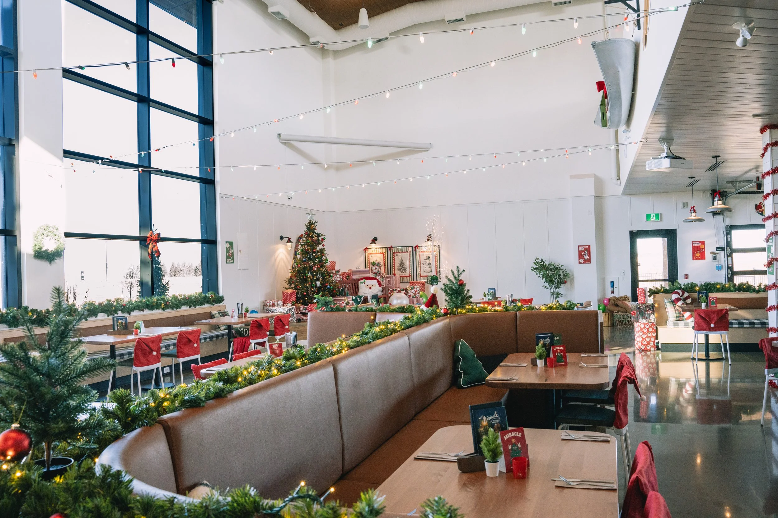 A decorated room with Christmas trees, wrapped gifts, and festive decorations, including string lights and holiday themed table settings, suggesting a Christmas celebration or holiday party.