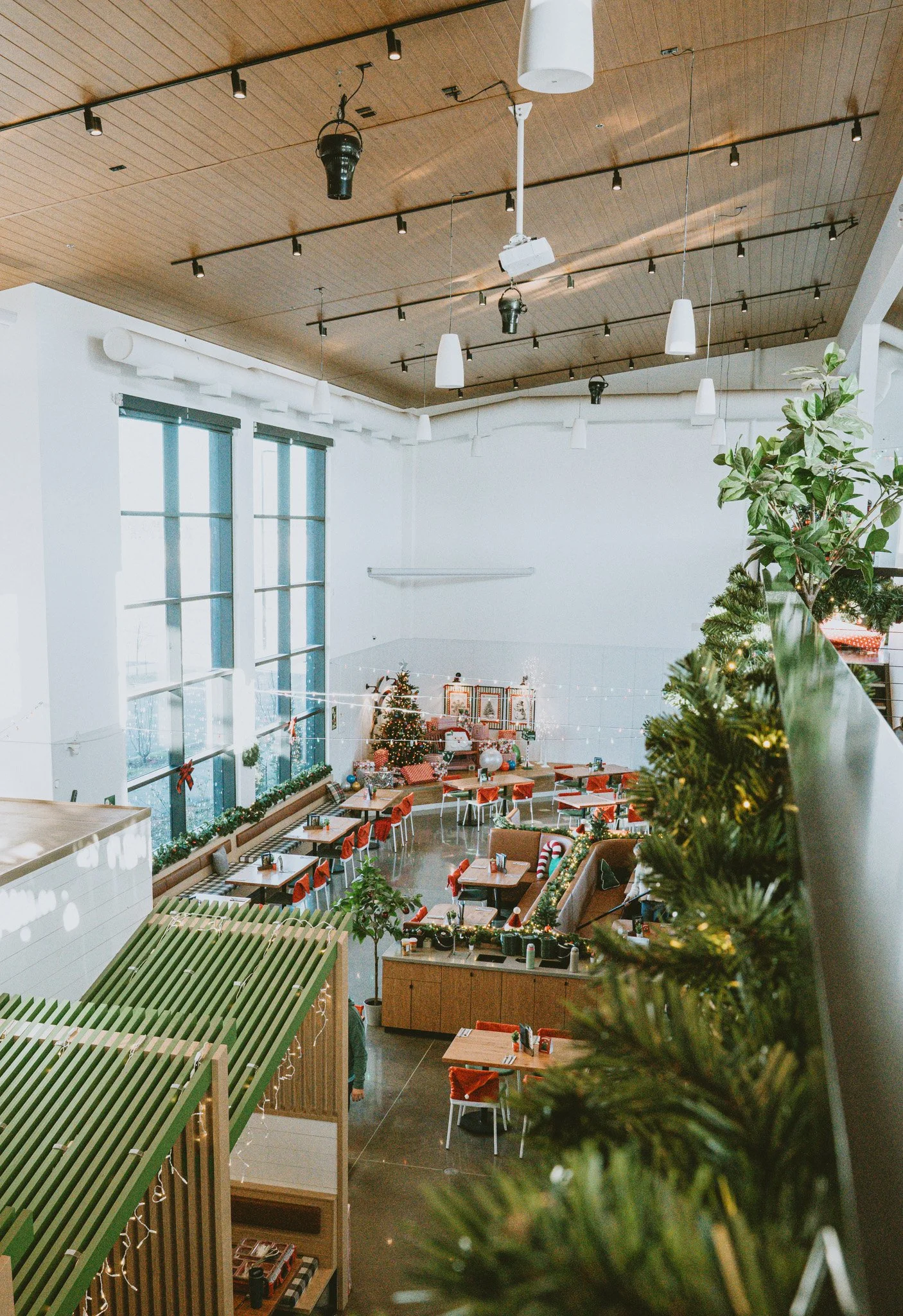 The image shows a decorated indoor space with Christmas elements, including a Christmas tree and Christmas stockings. The space has large windows with a view outside and is furnished with tables and chairs, suggesting it is a restaurant or cafe prepa