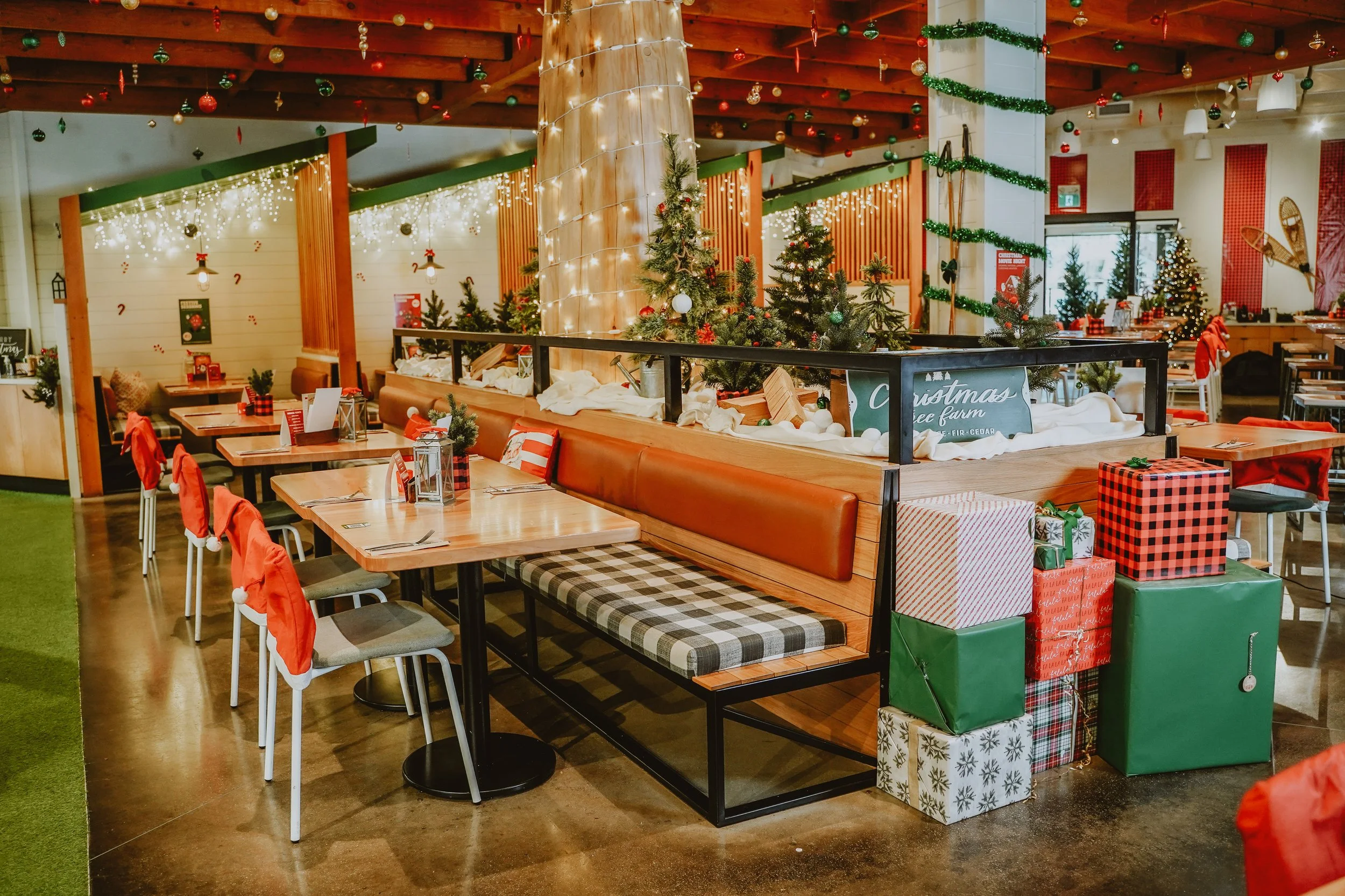 Decorated indoor space with Christmas trees, wrapped gifts, and festive decorations including string lights, ornaments, and garlands, suggesting a holiday celebration.