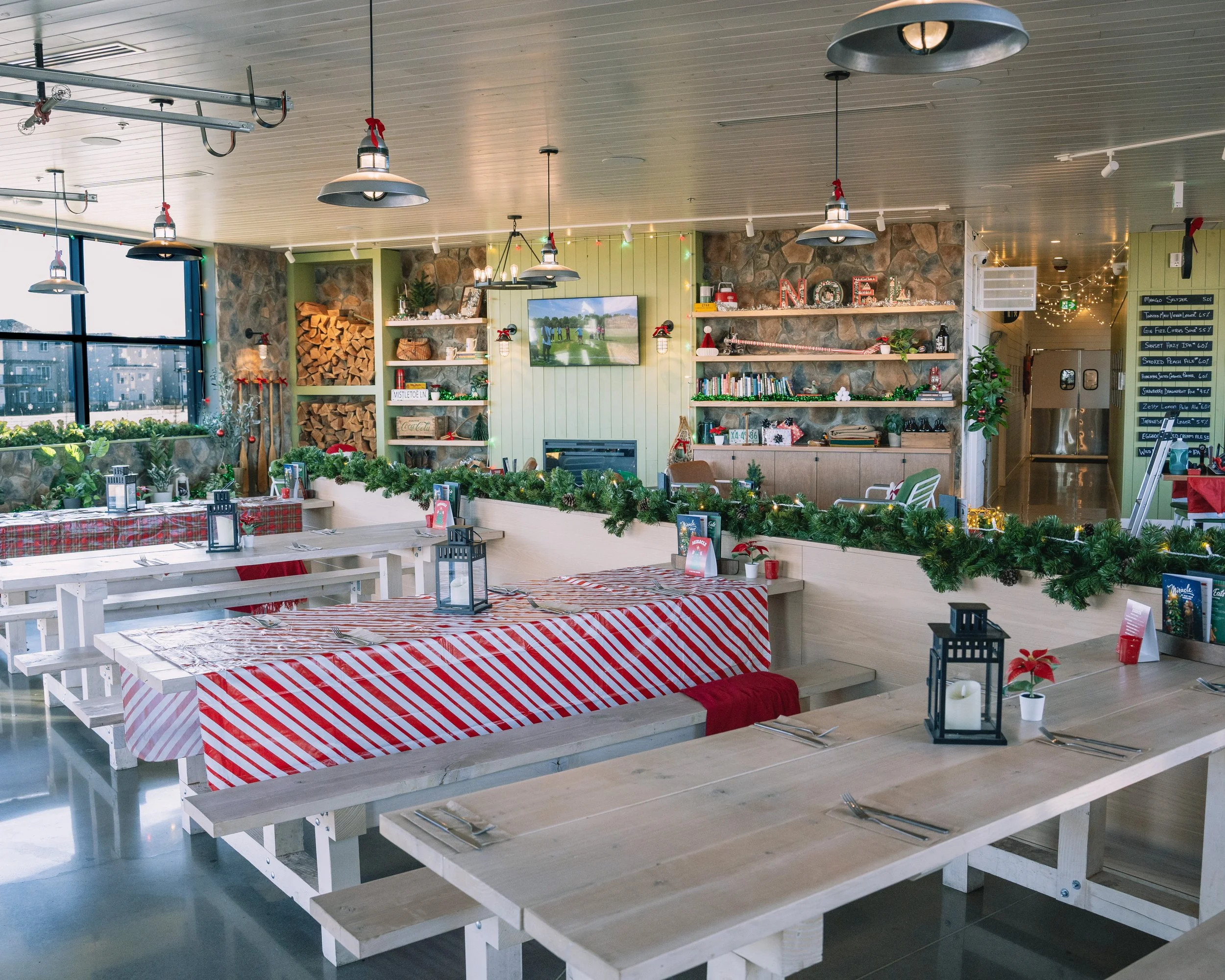 Indoor decorated restaurant or dining area with windows, Christmas decorations, hanging lights, shelves, and tables with red and white striped tablecloths.