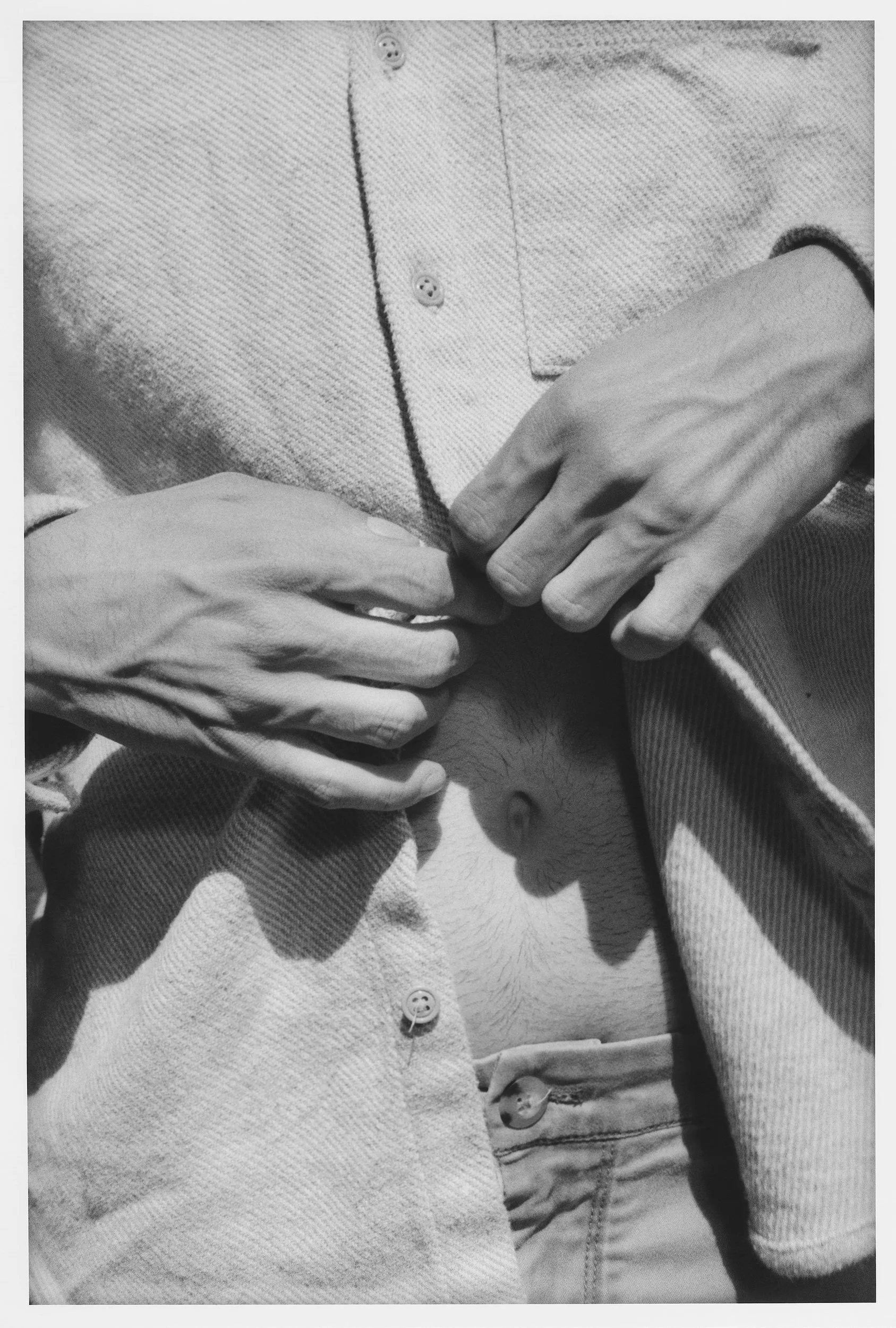 Black and white photo of two people holding each other, focusing on their hands and torsos. One person is wearing a textured, button-up shirt with rolled-up sleeves, and the other person is wearing a denim jacket and a t-shirt. Their hands are claspe