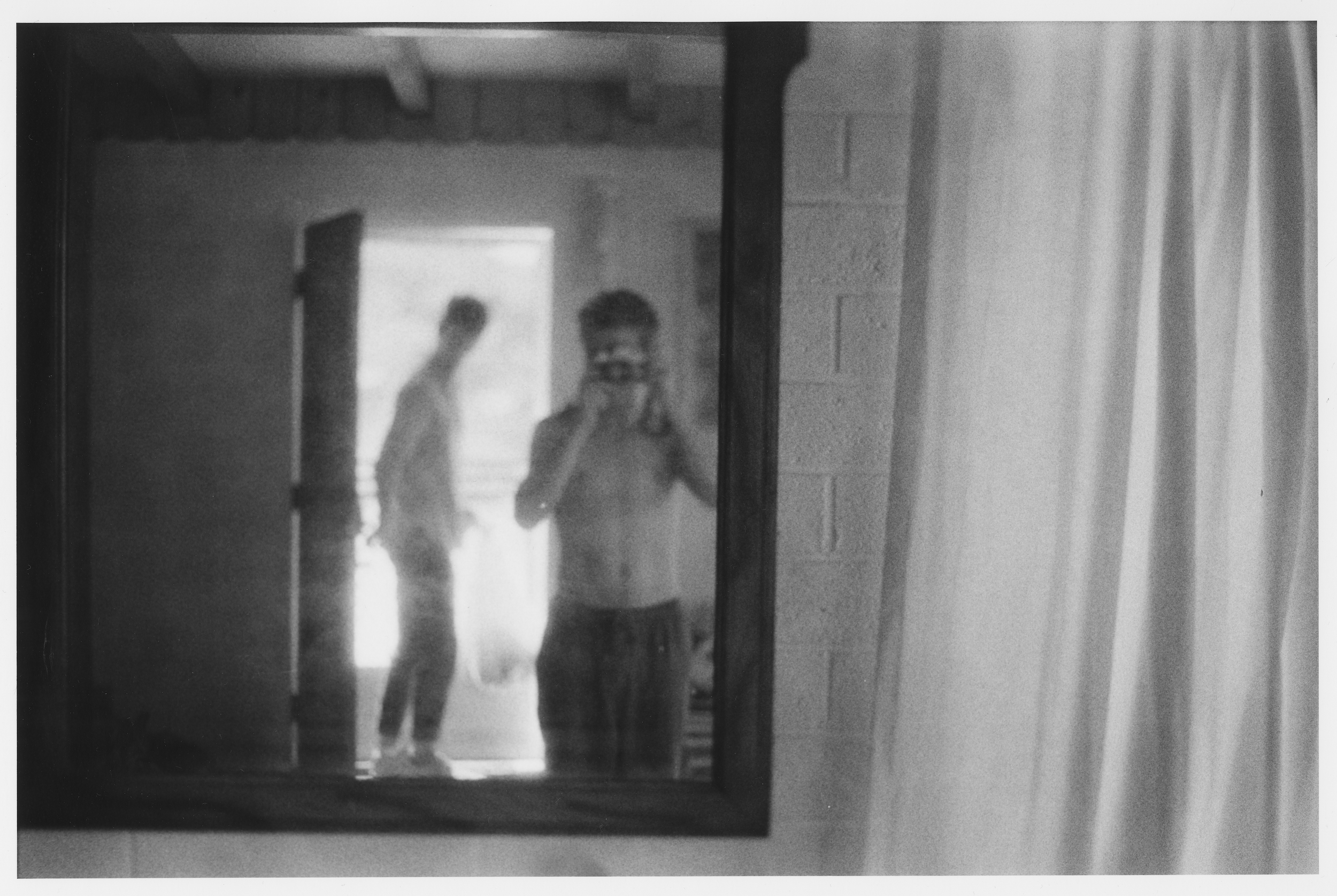 A black-and-white photo showing a person taking a selfie in a mirror. The person is standing on a staircase, with a stairway visible in the background. The person's reflection is the main focus, with blurred surroundings.