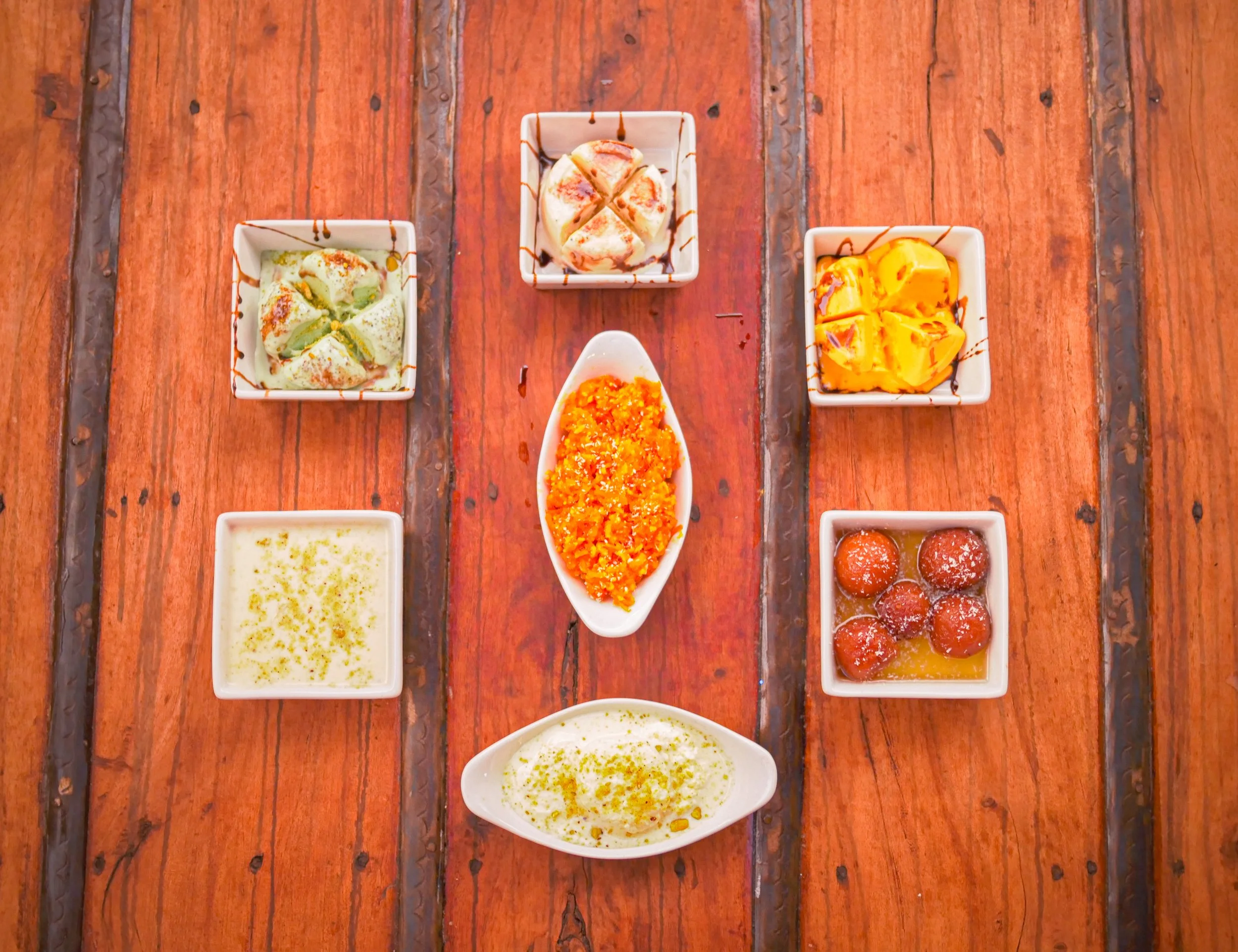 Assorted Indian desserts on a wooden table, including rabri, kulfi, falooda, and gulab jamun.