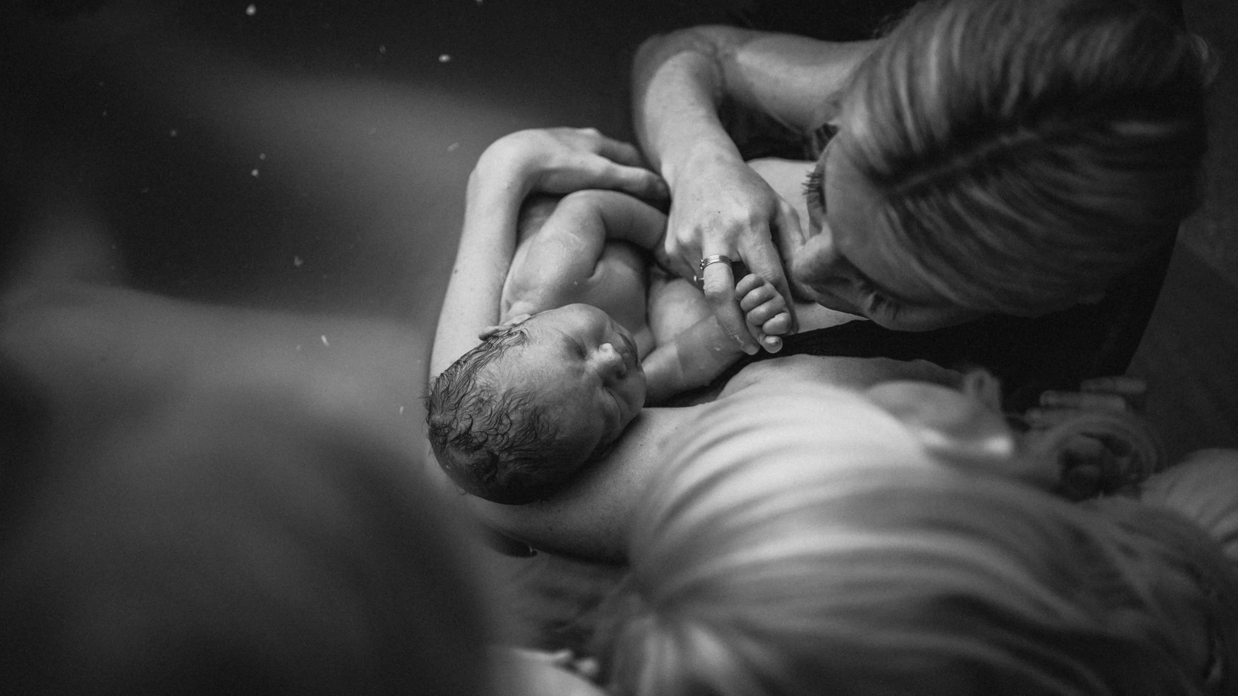 Children present at the birth of their brother look at the baby after mother gave birth in birth tub.
