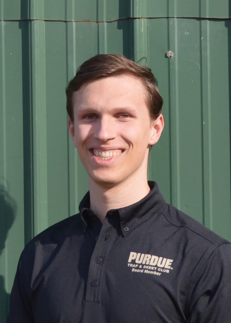 Smiling person wearing a black and gray shirt with a textured pattern, standing outdoors.