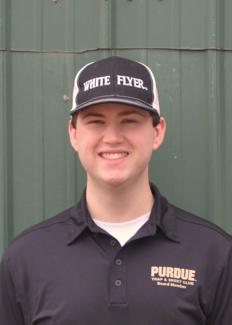 Young man smiling in front of a wooden fence, wearing a black T-shirt."
