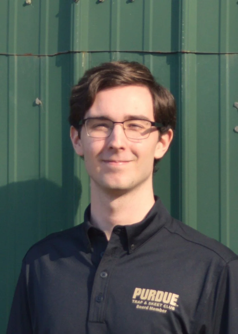 Person with long, wavy blonde hair smiling, wearing a shirt with text partially visible, possibly in an outdoor setting with a blurred background.