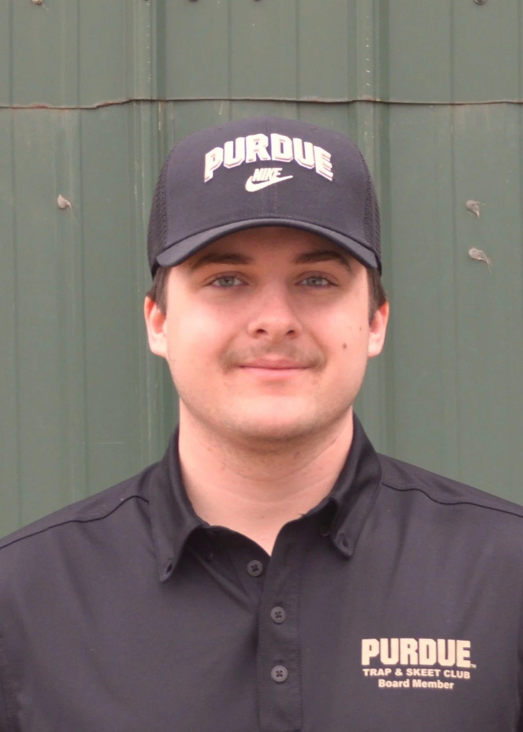 Person wearing a black cap and gray hoodie outdoors, smiling.