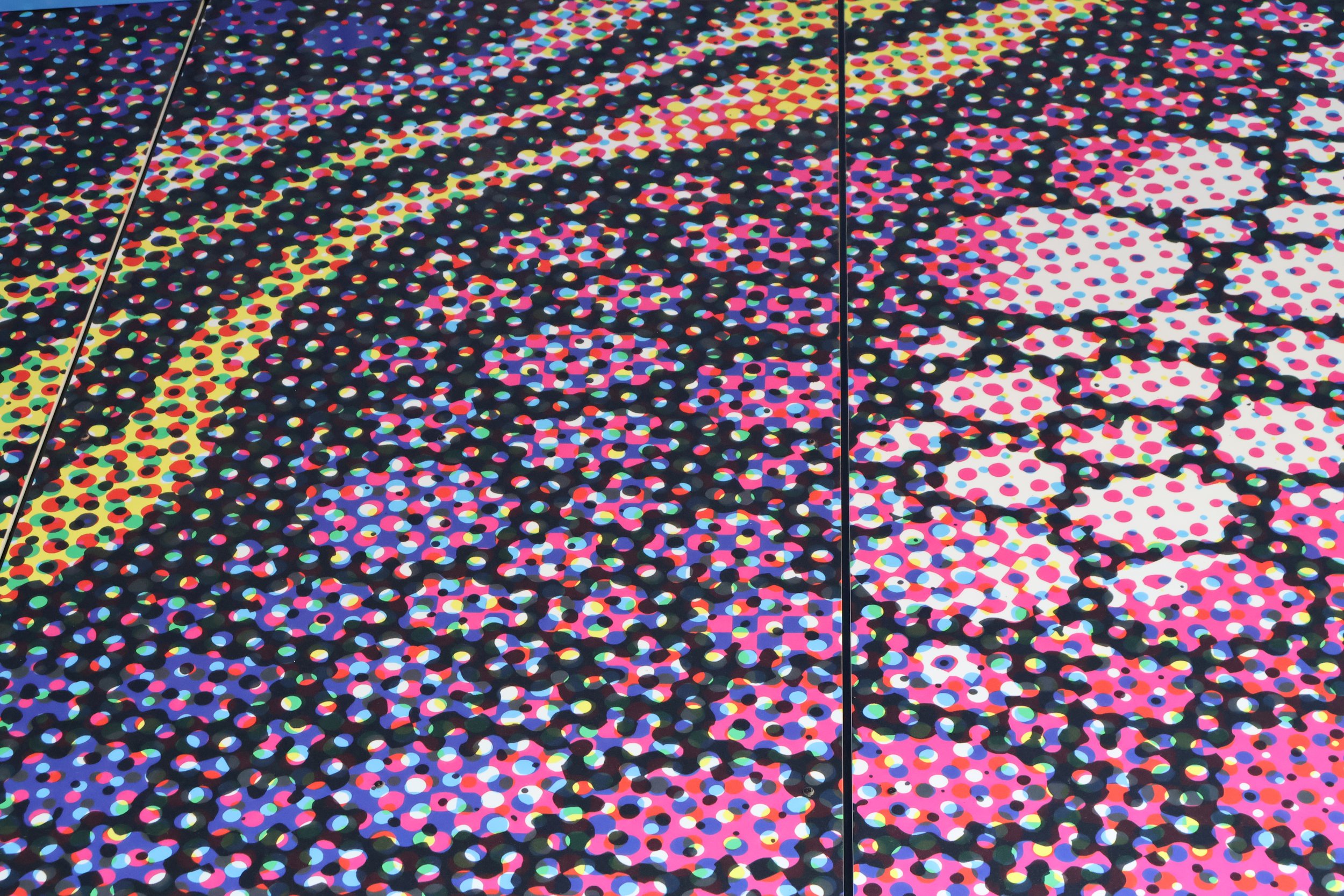 Colorful mosaic wall mural with swirling dot patterns and two black doors.