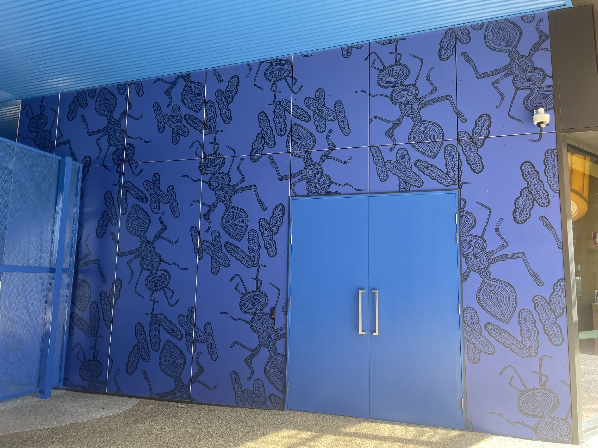 Blue wall with abstract line art of stylized ants and a door with silver handles.