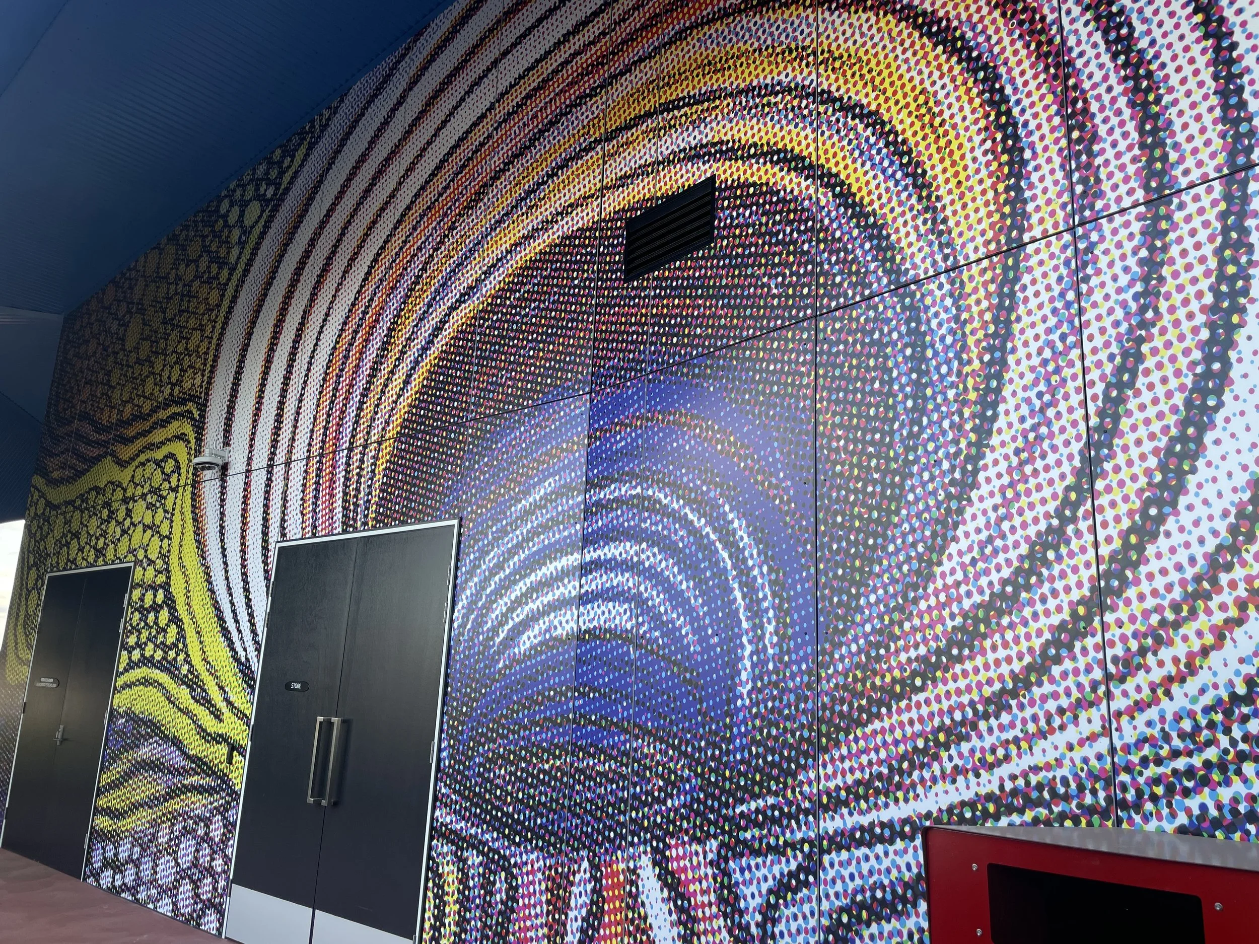 Colorful mosaic wall mural with swirling dot patterns and two black doors.