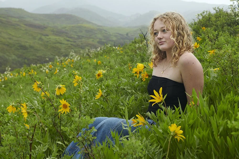 senior portrait teen girl sitting on mountainside in flowers fog