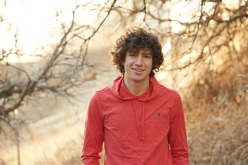 senior portrait of teenage curly haired boy in beautiful backlit fall scene